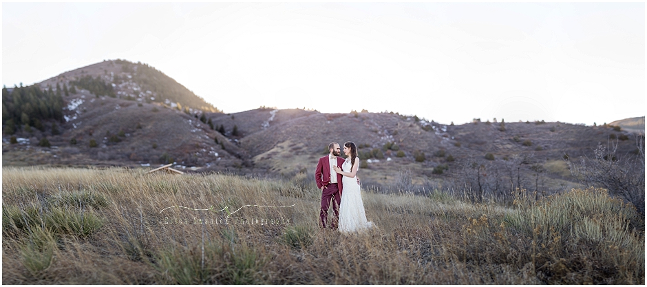 A groom in a burgundy suit stands with his bride in white as the sun sets behind them in the Colorado foothills for their country bohemian wedding. | Erica Swantek Photography