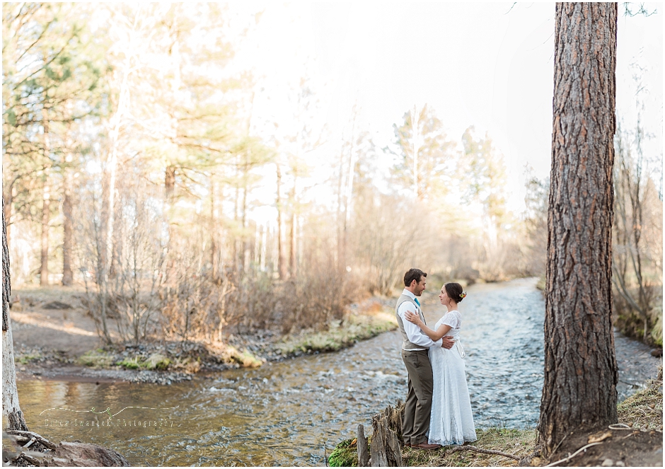 A couple stands facing each other in their wedding attire as the sun sets behind them along Wychus Creek at their backyard wedding in Sisters, Oregon. | Erica Swantek Photography