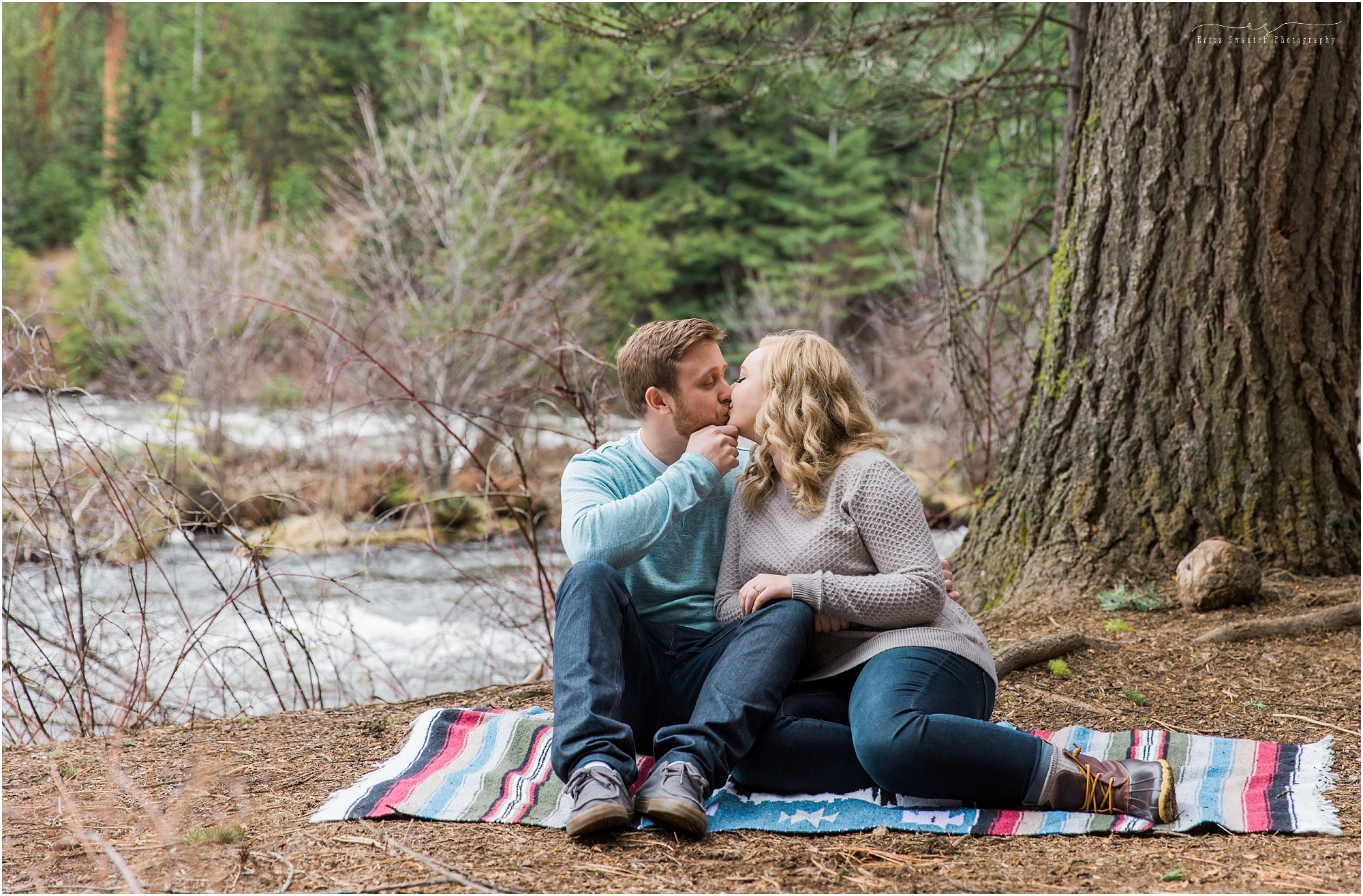 A sweet couple sits on a blanket along the banks of the mighty Deschutes River for their spring Bend, OR engagement session. 