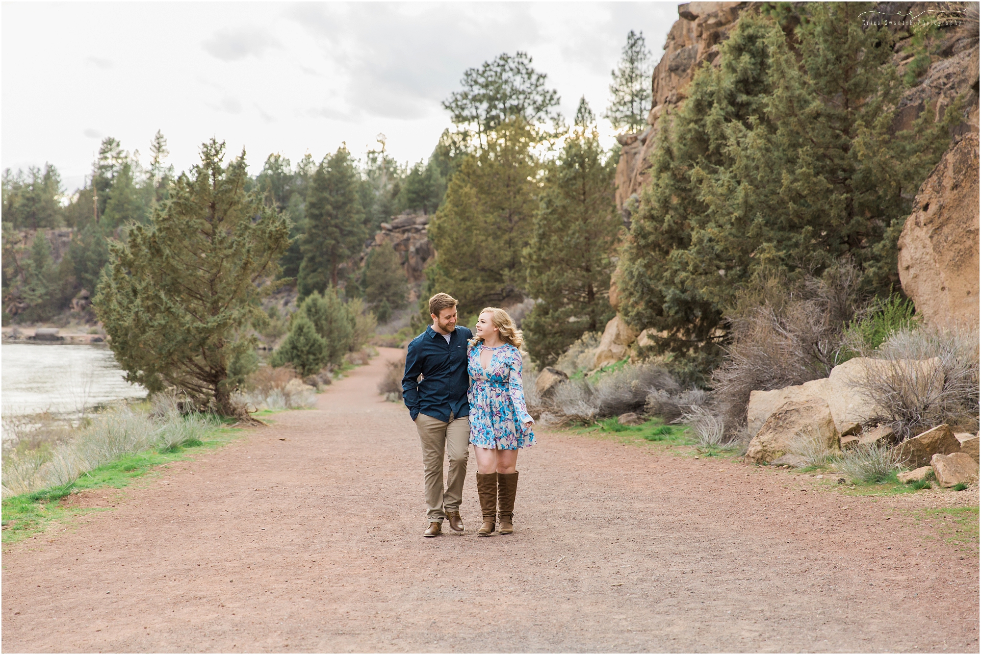A couple wearing blue walks along the Deschutes River trail near the Old Mill District in Bend, Oregon for their spring engagement session. | Erica Swantek Photography