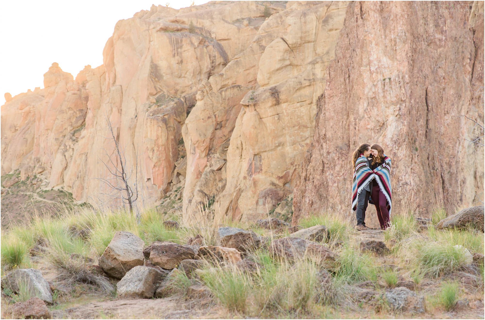 A cute couple cuddles up under a blanket as the sun sets at their Smith Rock Engagement Session. | Erica Swantek Photography 