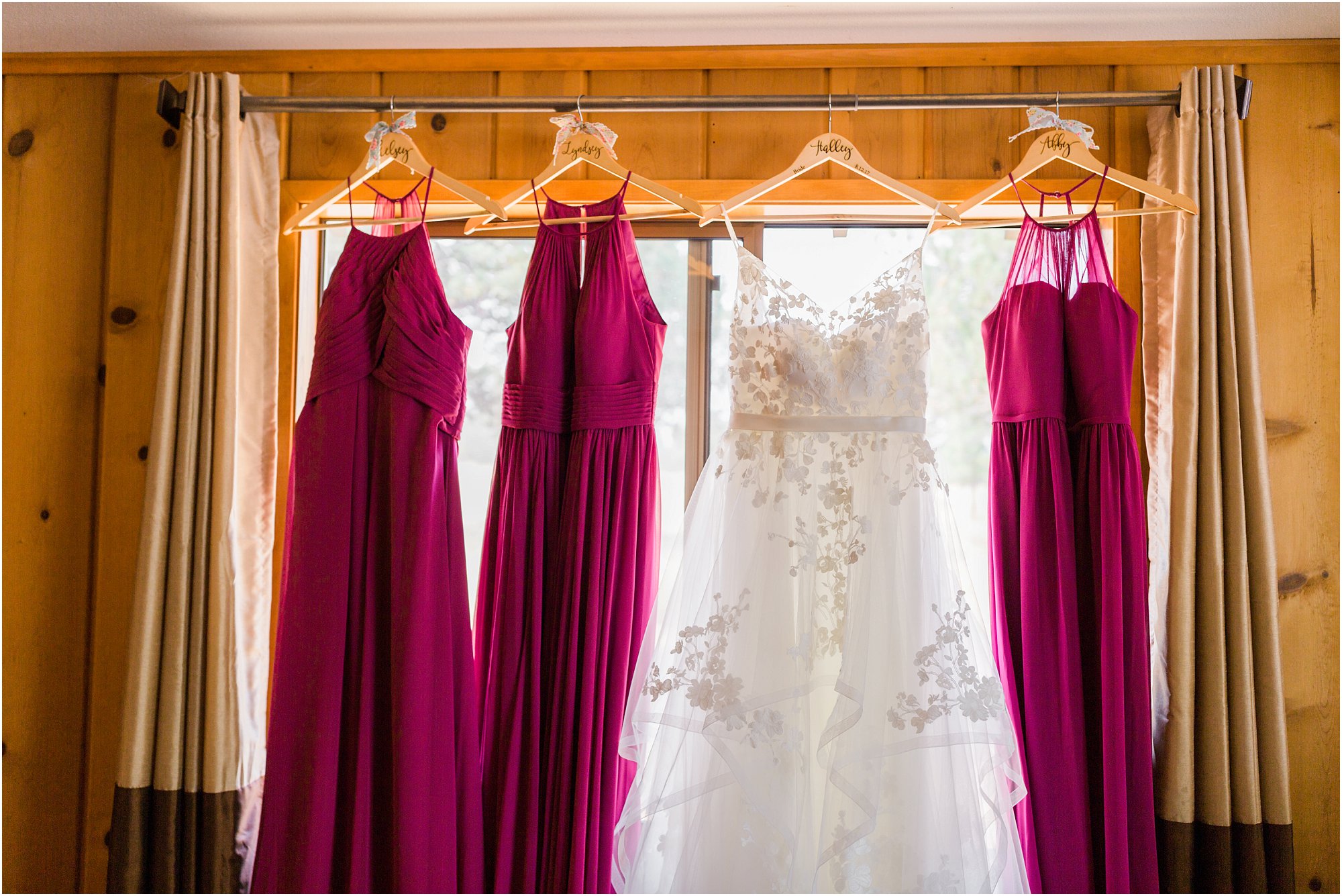 A gorgeous Beloved by Casablanca wedding gown next to magenta bridesmaid dresses in the window of the rustic Rock Springs Ranch wedding venue by Bend wedding photographer Erica Swantek Photography. 