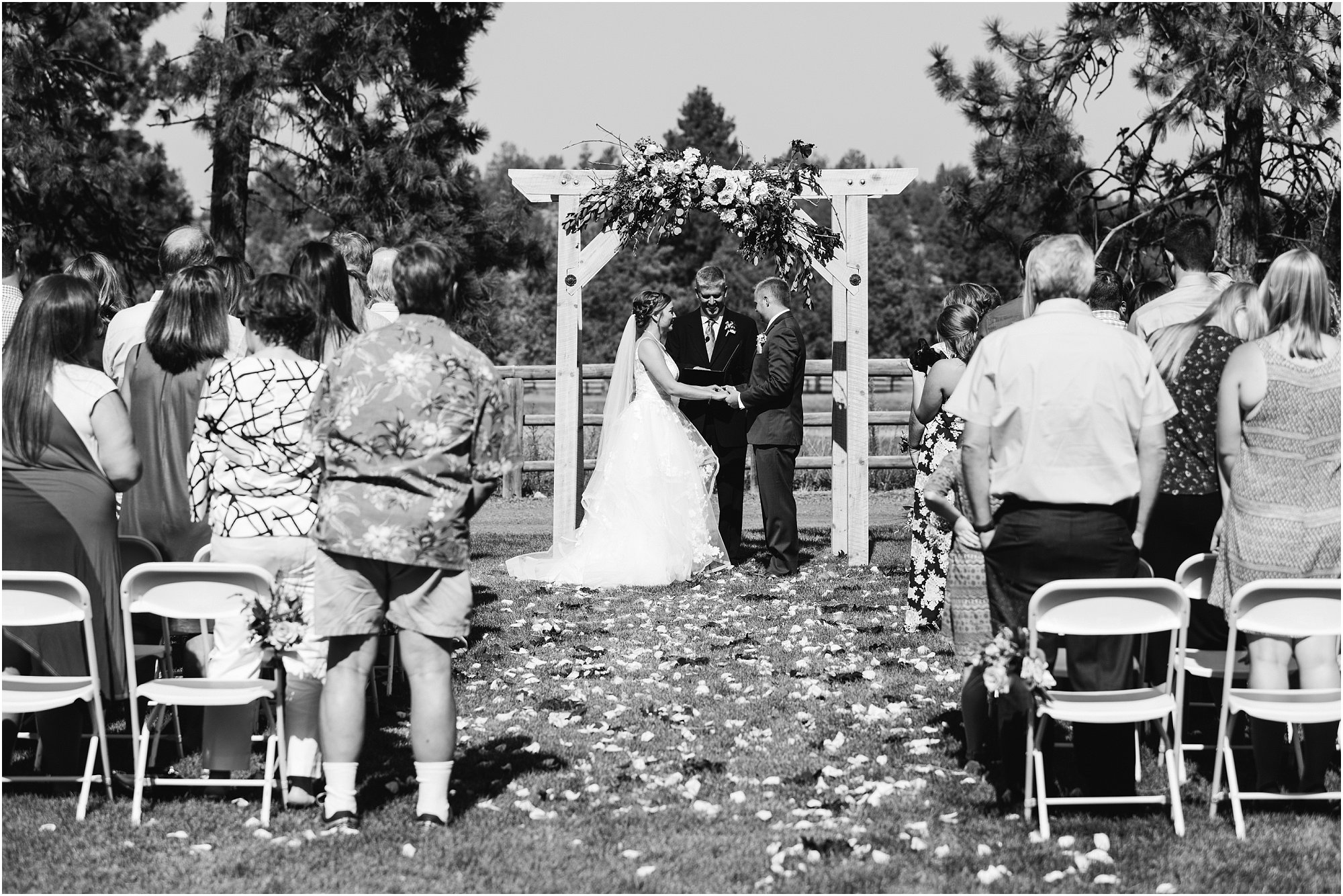 A beautiful black and white photograph of the bride and groom standing at the flower draped wedding arch during their outdoor ceremony at Rock Springs Ranch in Bend, OR. | Erica Swantek Photography
