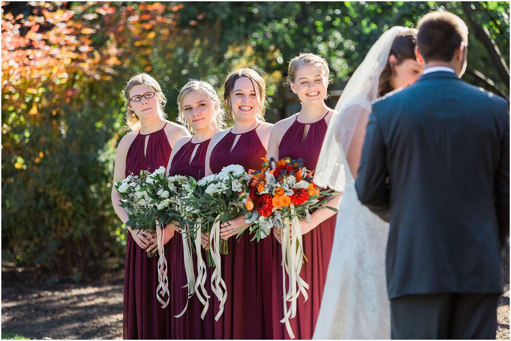 Bridesmaids wearing gorgeous maroon Bill Levkoff gowns look on as the happy couple exchances their vows at their outdoor fall wedding in Bend, OR. | Erica Swantek Photography