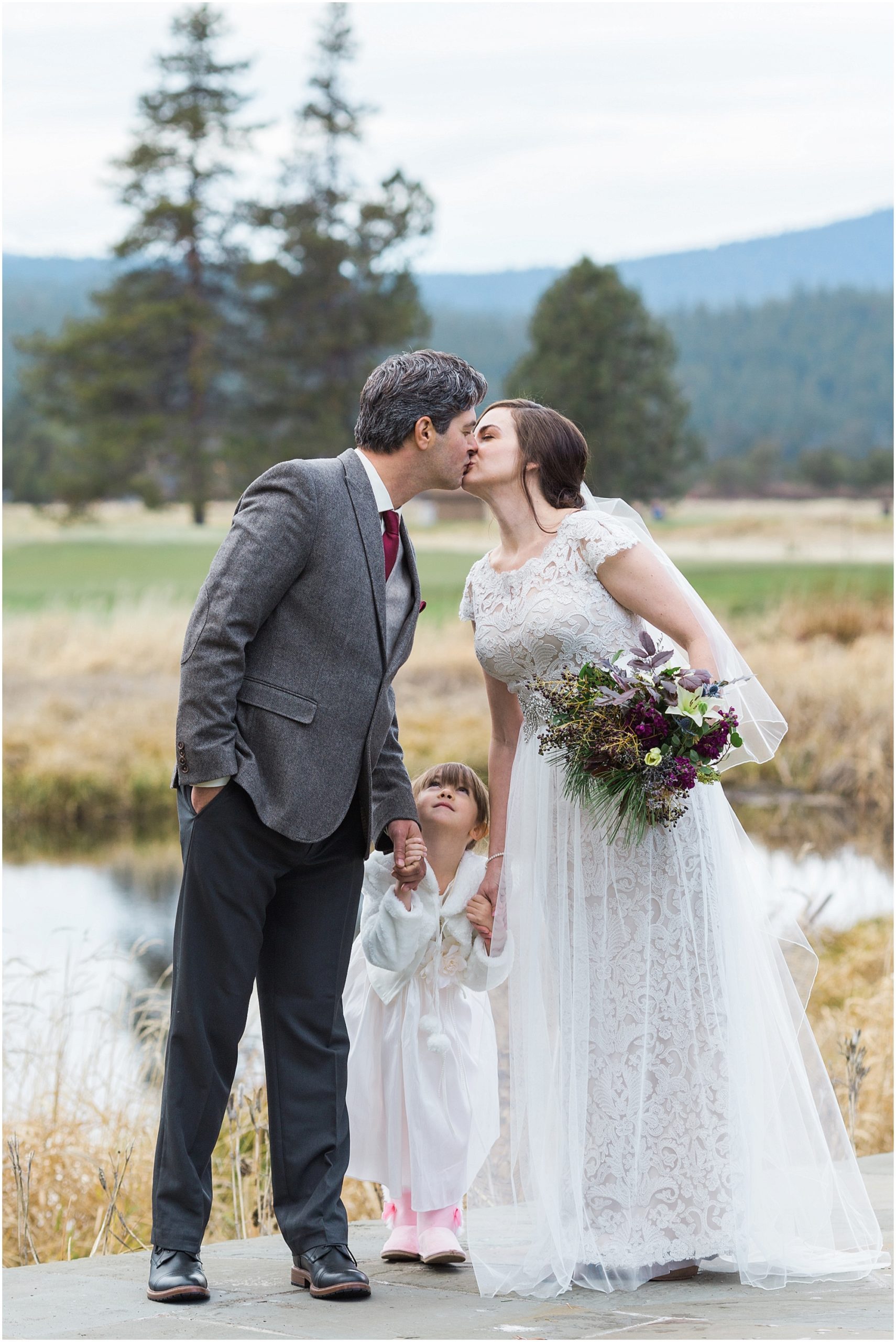 An adorable family portrait of the newly married couple kissing while their young daughter glances up all smiles at this wedding at Sunriver Resort in Oregon. | Erica Swantek Photography