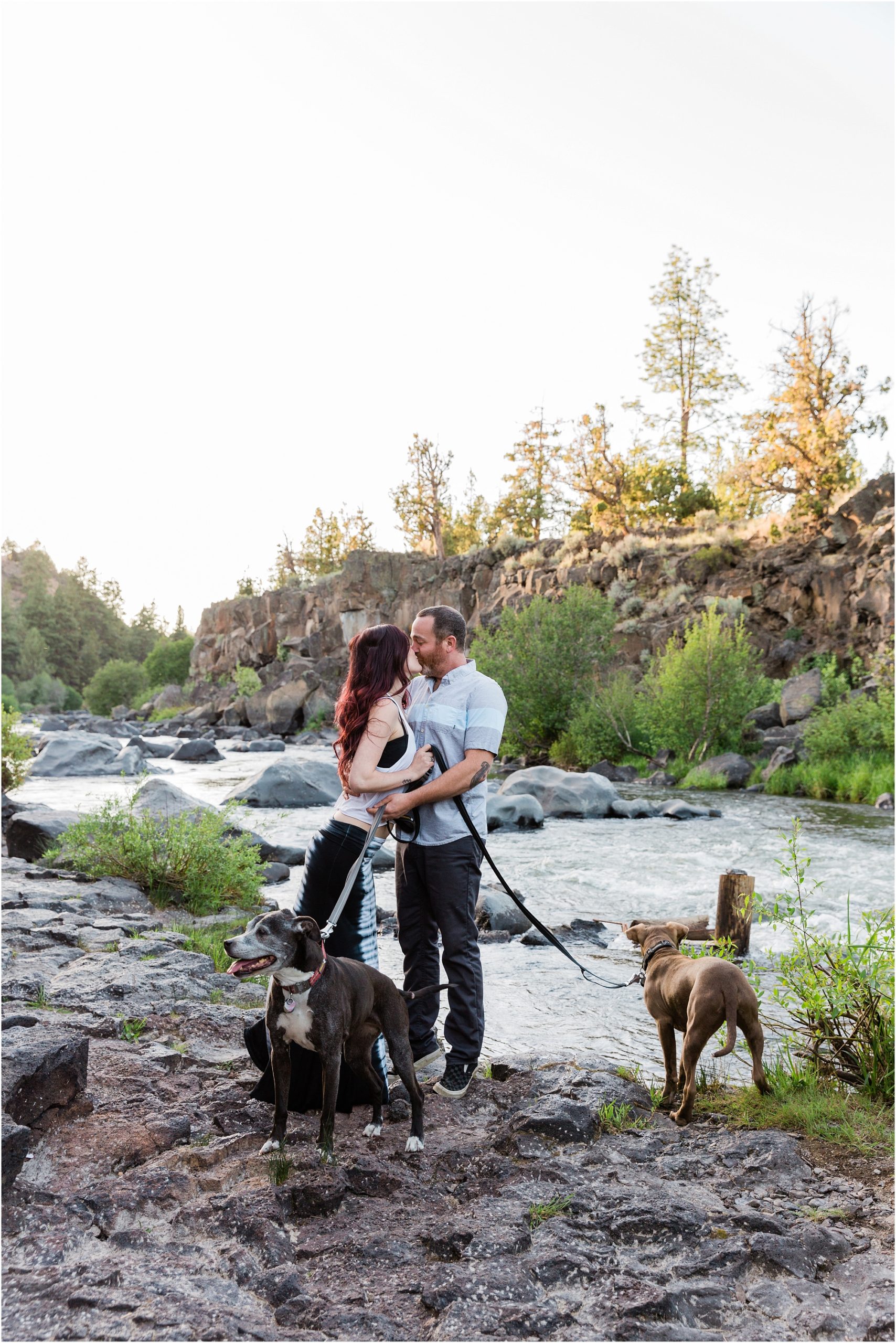 A gorgeous couple, along with their two dogs, pose along the Deschutes River in Sawyer Park for this Bend engagement session with dogs in Oregon. | Erica Swantek Photography