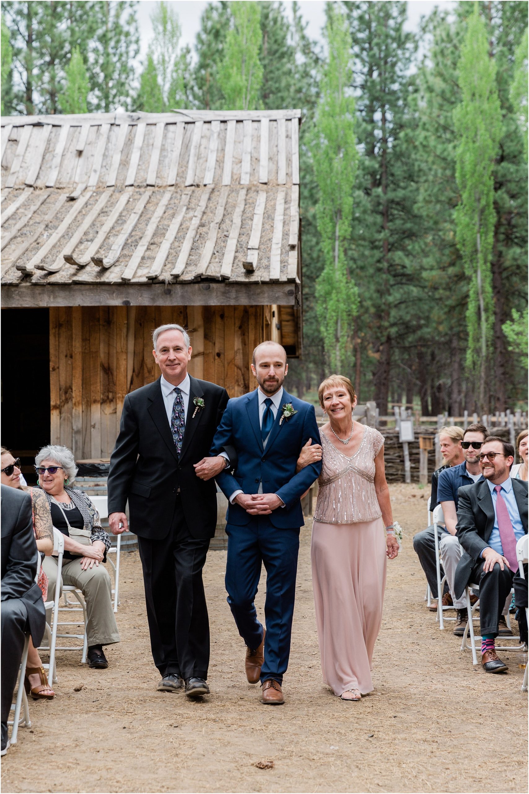 The groom escorts his parents down the dirt aisle wearing his cobalt blue suit as he prepares for his wedding ceremony in Bend, OR. | Erica Swantek Photography