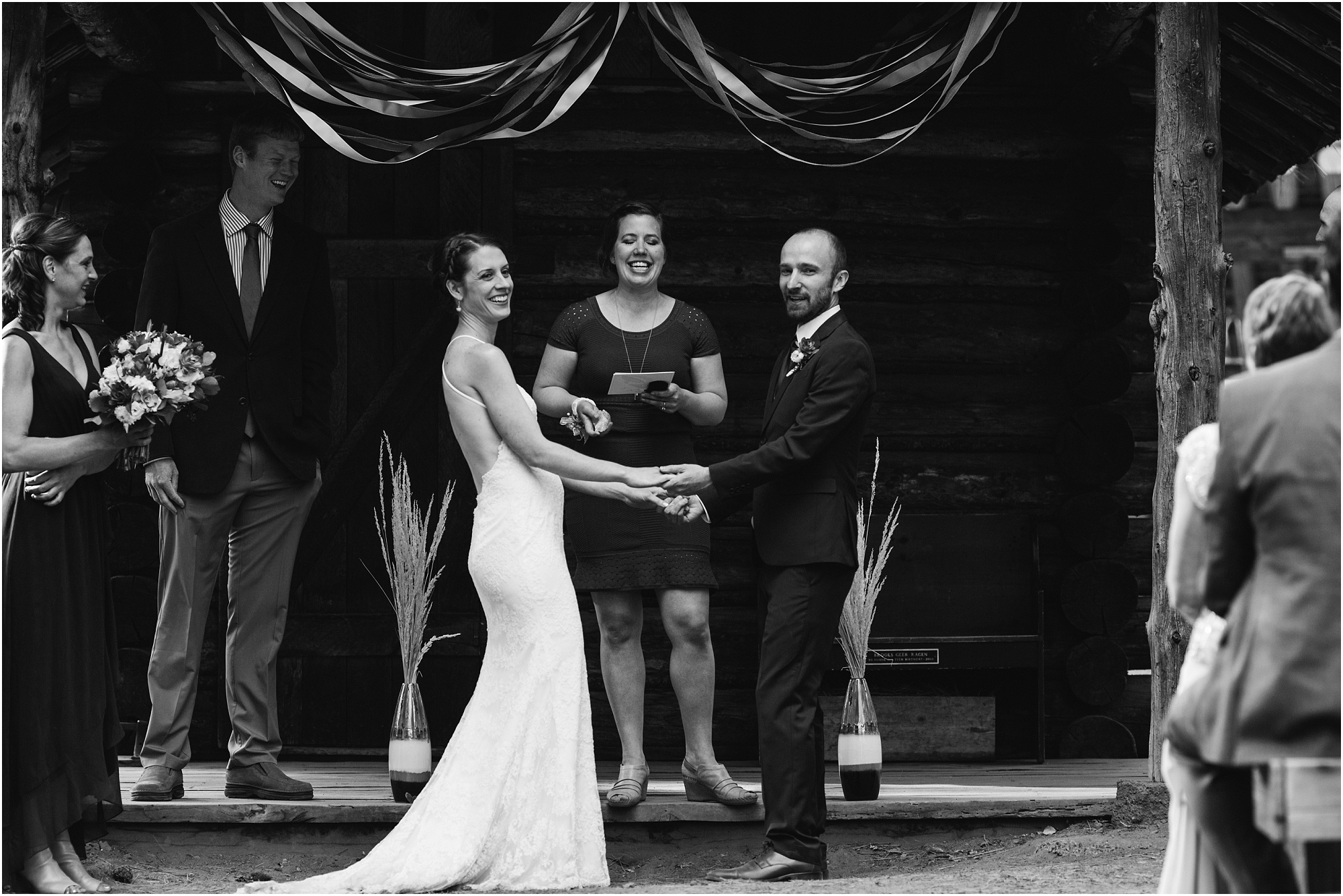 A beautiful black and white image of the bride and groom holding hands and smiling at their wedding guests during their rustic outdoor ceremony at the High Desert Museum wedding venue in Bend, OR. | Erica Swantek Photography