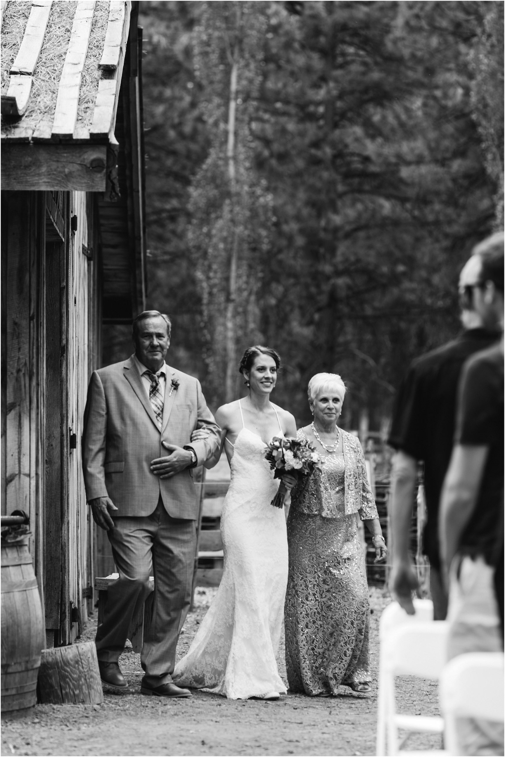 The bride, wearing a strappy BHLDN gown, is escorted by her parents down the dirt aisle at her rustic outdoor wedding at Bend, Oregon's High Desert Museum. | Erica Swantek Photography