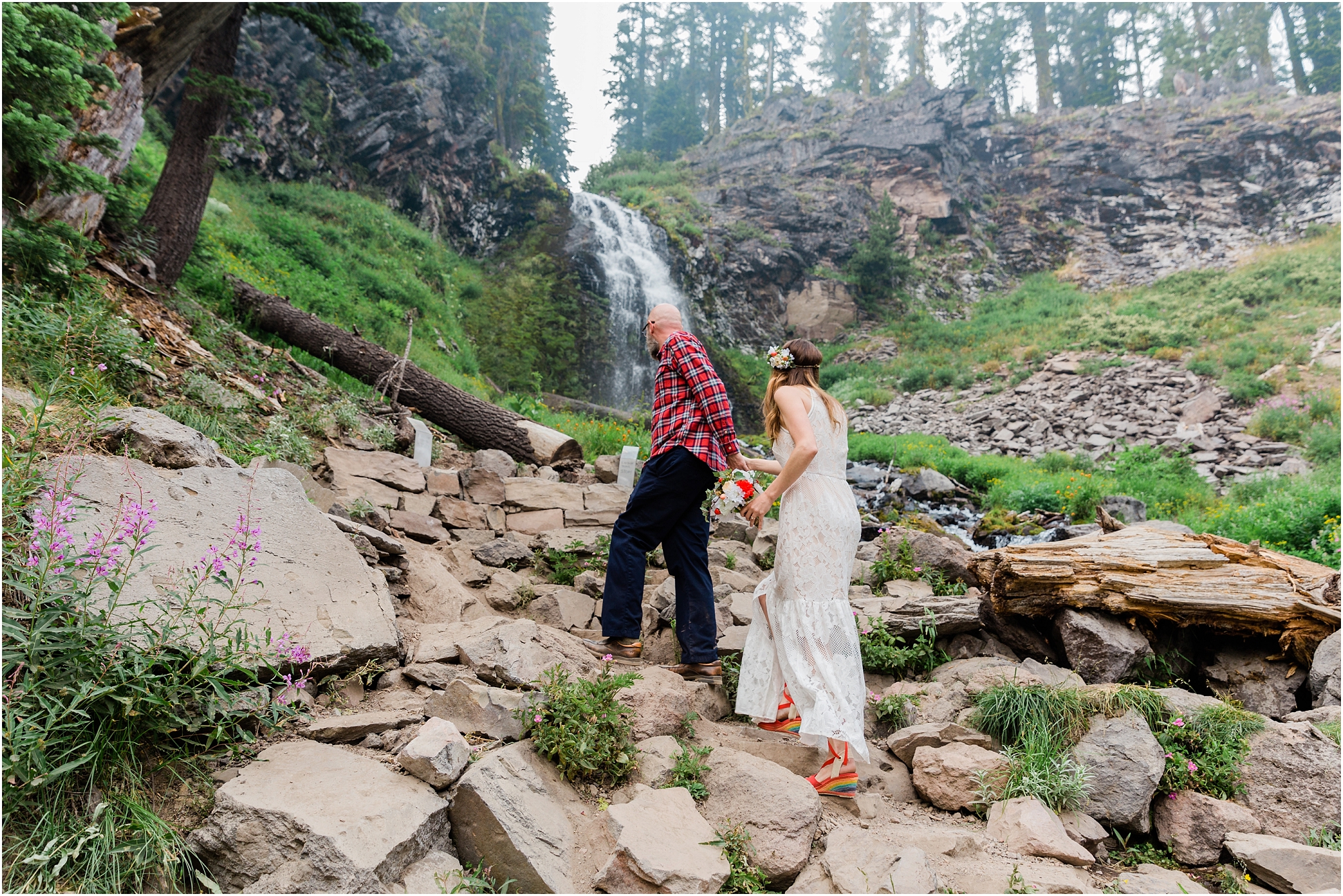 A groom wearing a red plaid shirt, and a bohemian bride with a floral crown and rainbow heels, approaches the ceremony site for their Crater Lake elopement in Oregon. | Erica Swantek Photography