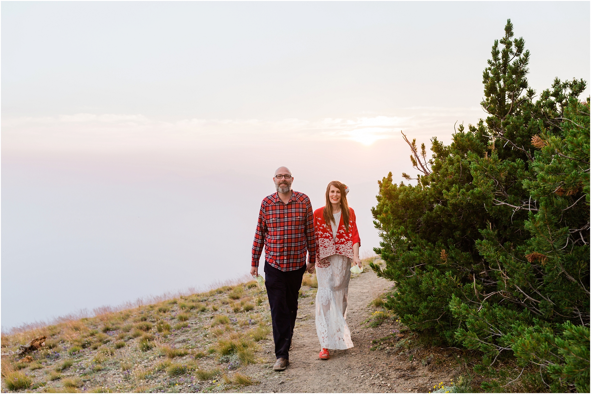 The sun starts dipping below the smoke, creating hazy glowing light as this couple hikes along the trail for their elopement at Crater Lake National Park in Oregon. | Erica Swantek Photography