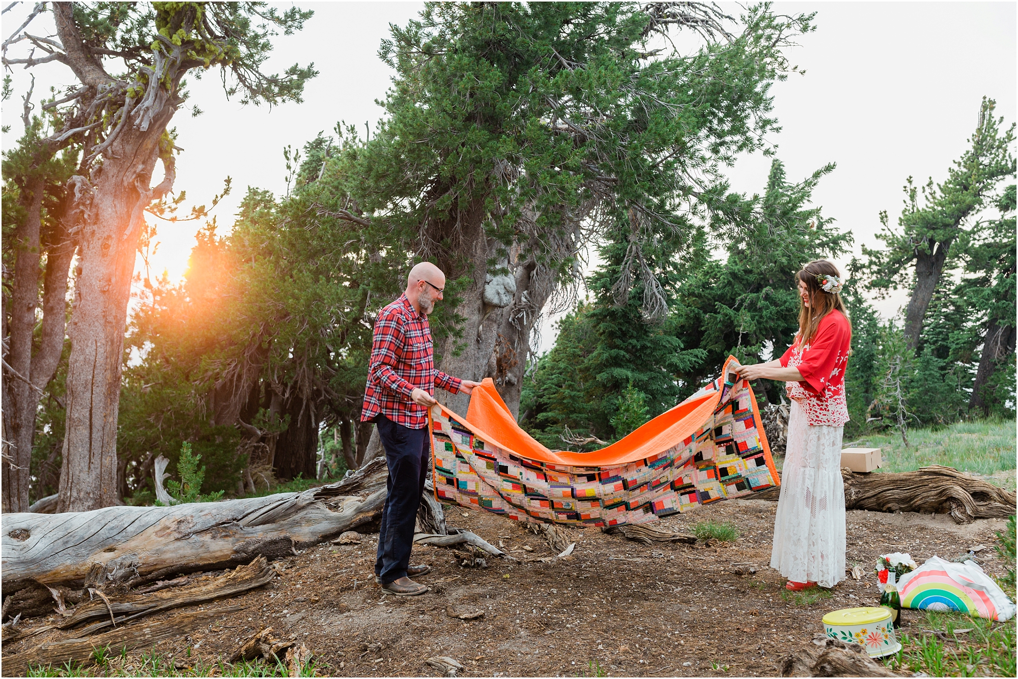The sun sets through the trees as this wedding couple gathers and folds their heirloom quilt and vintage decor they used at their Crater Lake elopement in Oregon. | Erica Swantek Photography