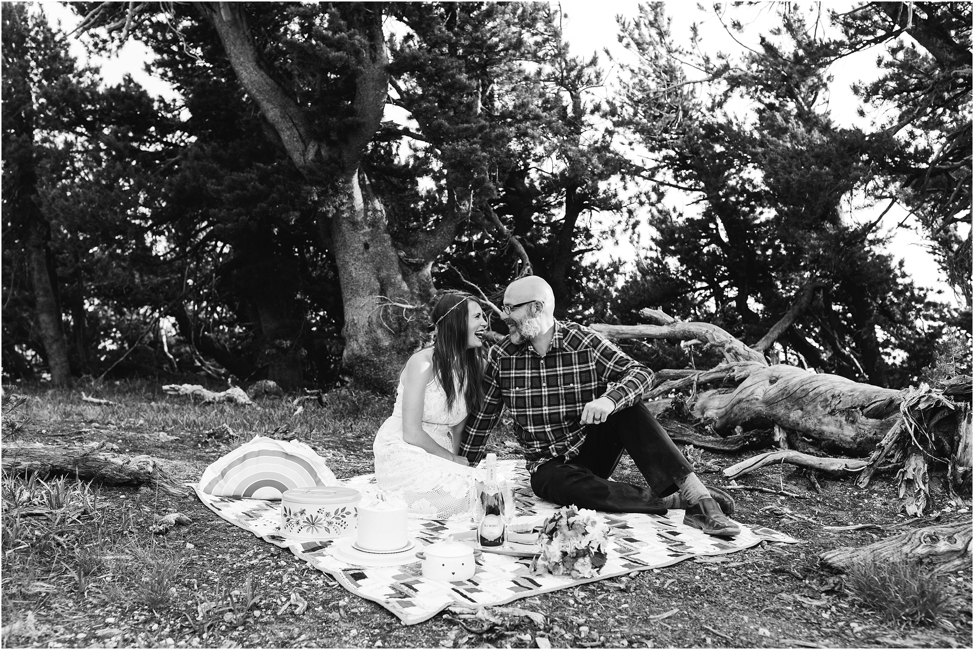 A black and white photo of a couple enjoying their picnic toast and wedding cake after they eloped at Crater Lake in Oregon. | Erica Swantek Photography