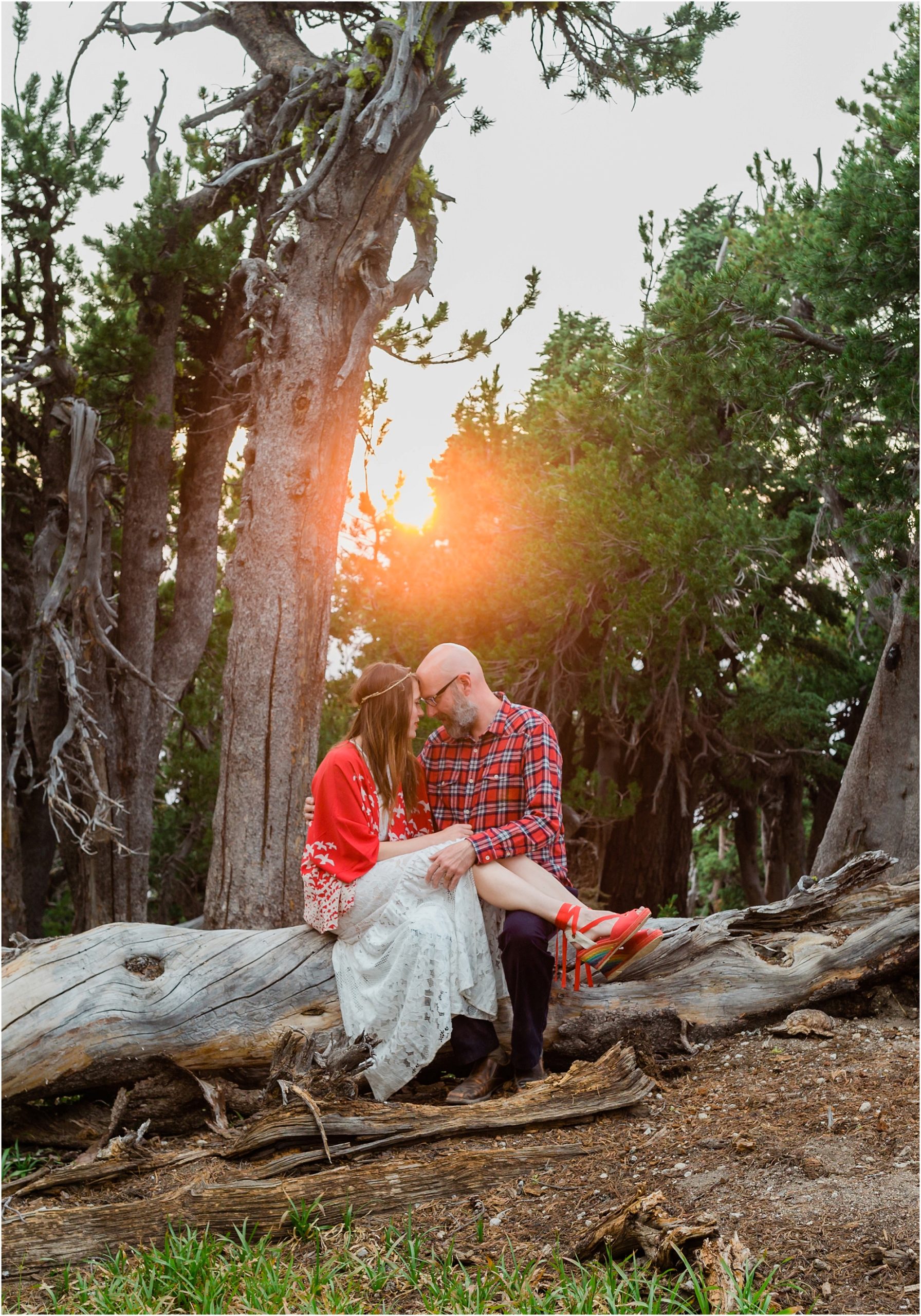 A bride drapes her legs over her groom, as they pose forehead to forehead with the sun setting behind them through the trees at their Crater Lake elopement in Oregon. | Erica Swantek Photography