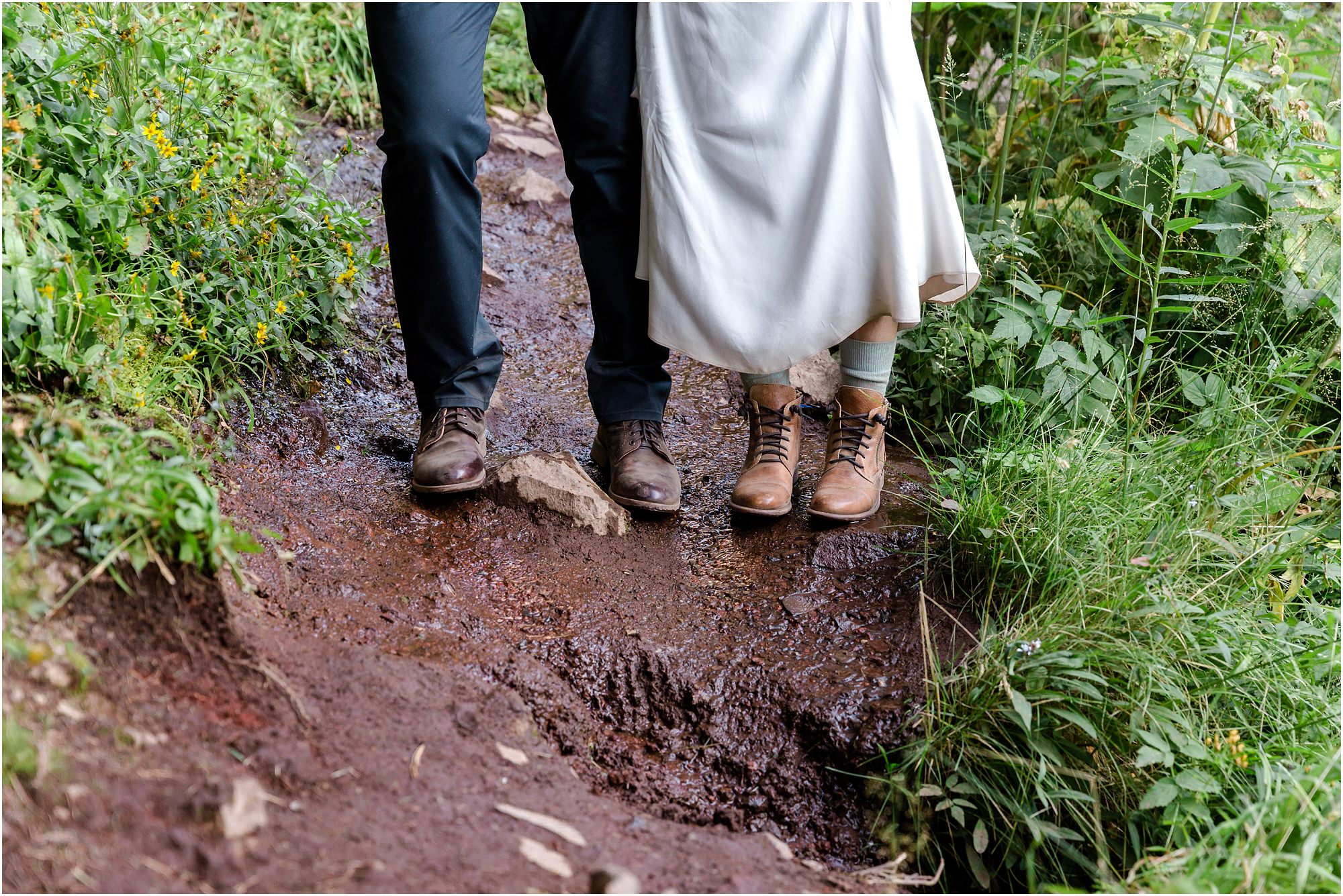 A bride wears hiking boots and lifts her dirty white dress in the mud on the trail to the waterfall during their Tumalo Falls elopement adventure photo session. | Erica Swantek Photography