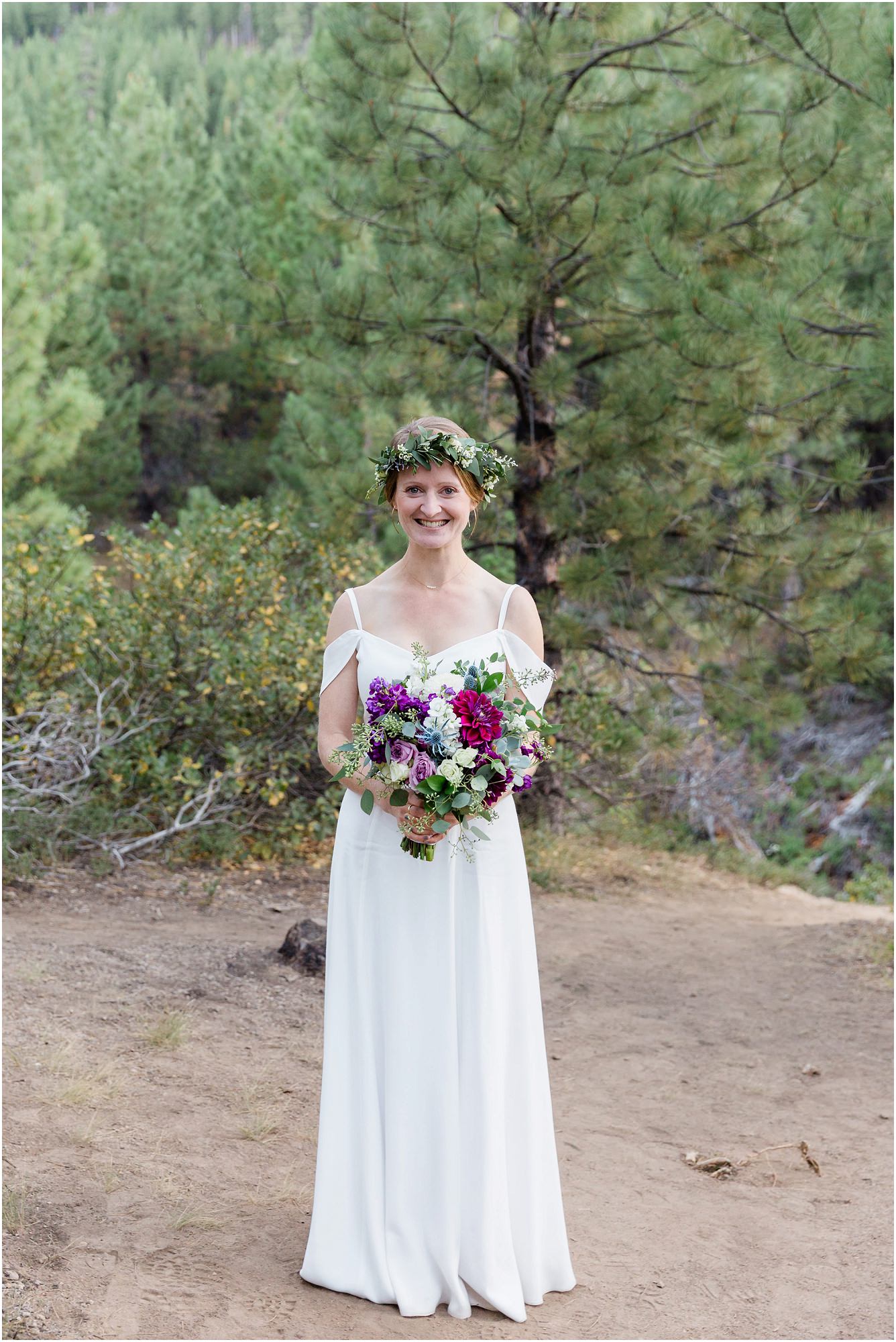 A gorgeous bride wearing a white flutter sleeve dress holds a bouquet of purple dahlias and green succulents while wearing a flower crown made of eucalyptus leaves and baby's breath at her Bend Oregon elopement. | Erica Swantek Photography 