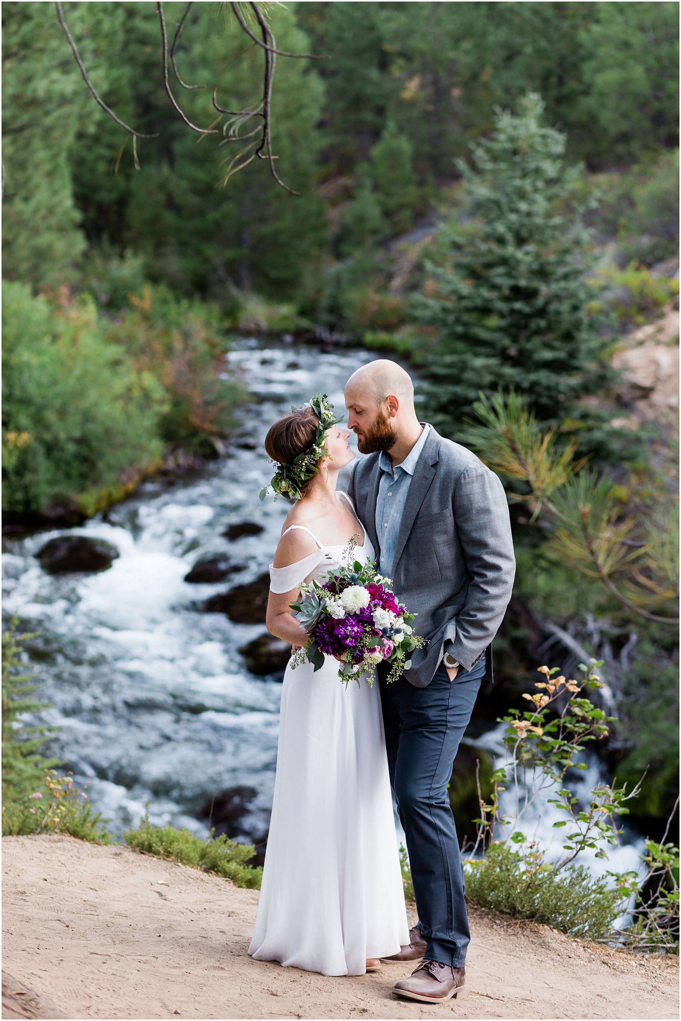 A gorgeous view of Tumalo Creek behind the bride wearing a white flutter sleeve dress and the groom is navy blue at their Tumalo Falls elopement near Bend, Oregon. | Erica Swantek Photography