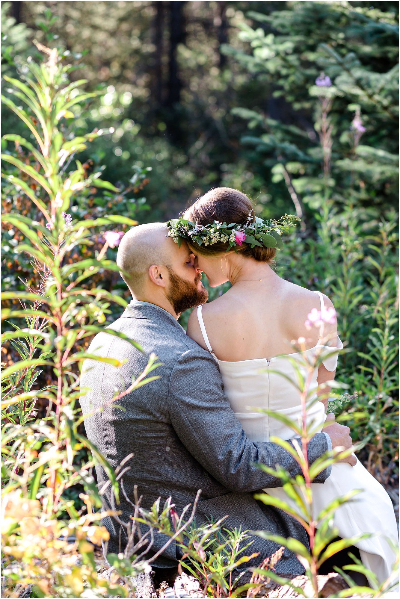 A bride sits on her groom's lap in the wildflowers and kisses her groom at their Bend Oregon elopement. | Erica Swantek Photography
