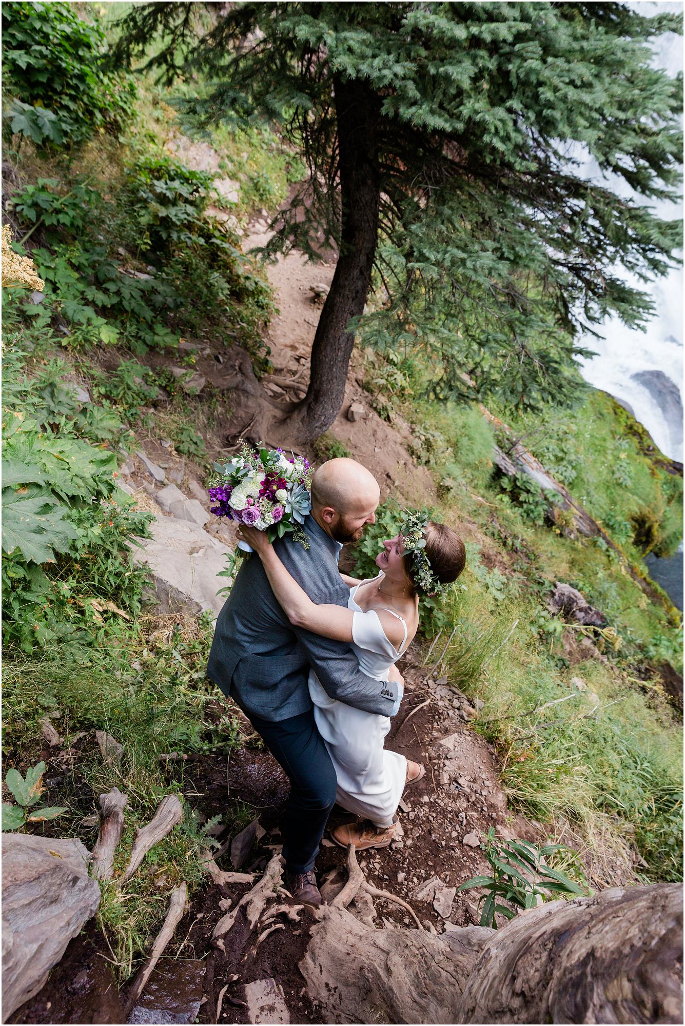 A groom lifts his bride down the steep trail near the waterfall during their adventurous hiking elopement in Bend, OR. | Erica Swantek Photography