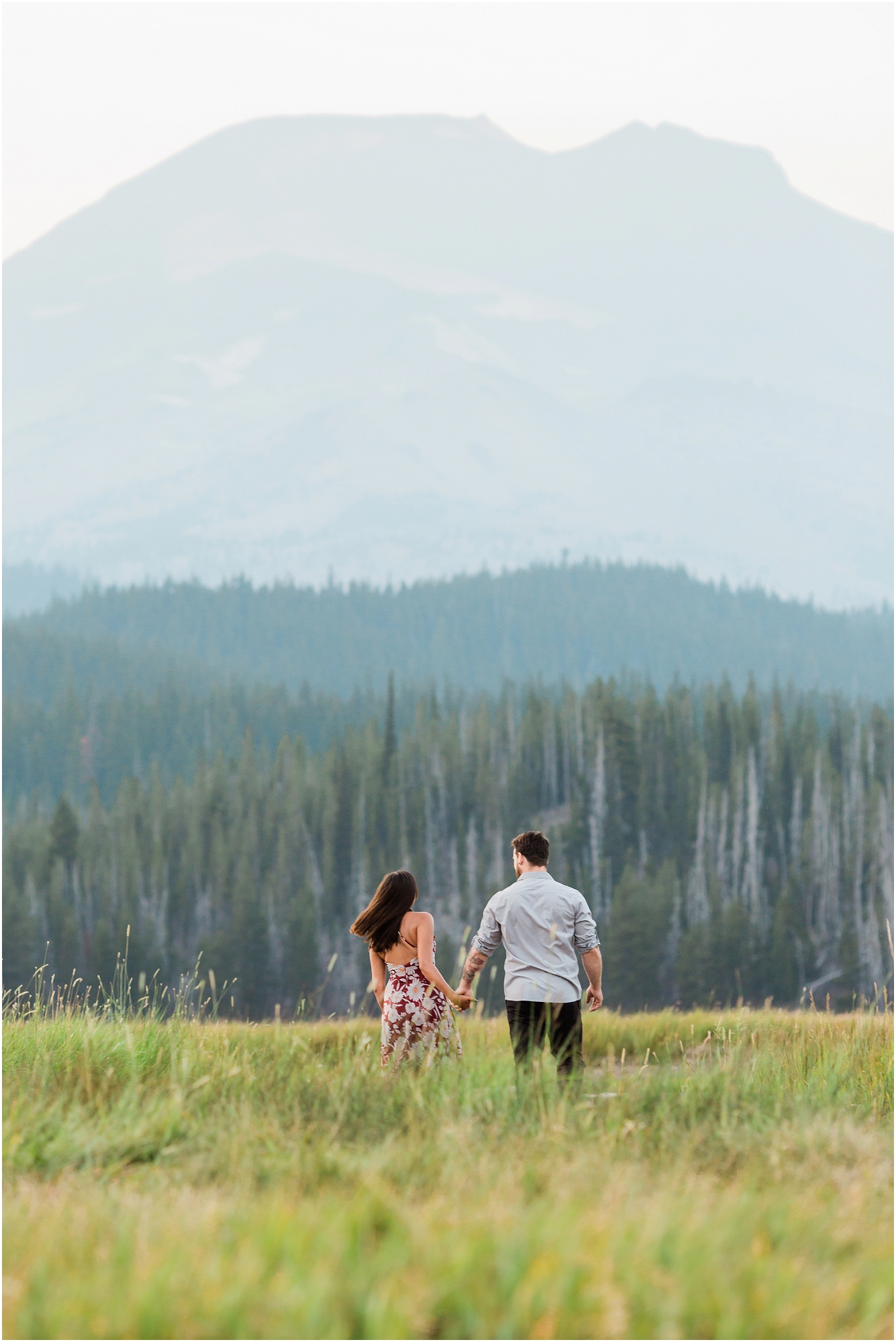 South Sister stands tall over a gorgeous meadow as a couple runs through the field at their Bend Oregon engagement photo session. | Erica Swantek Photography