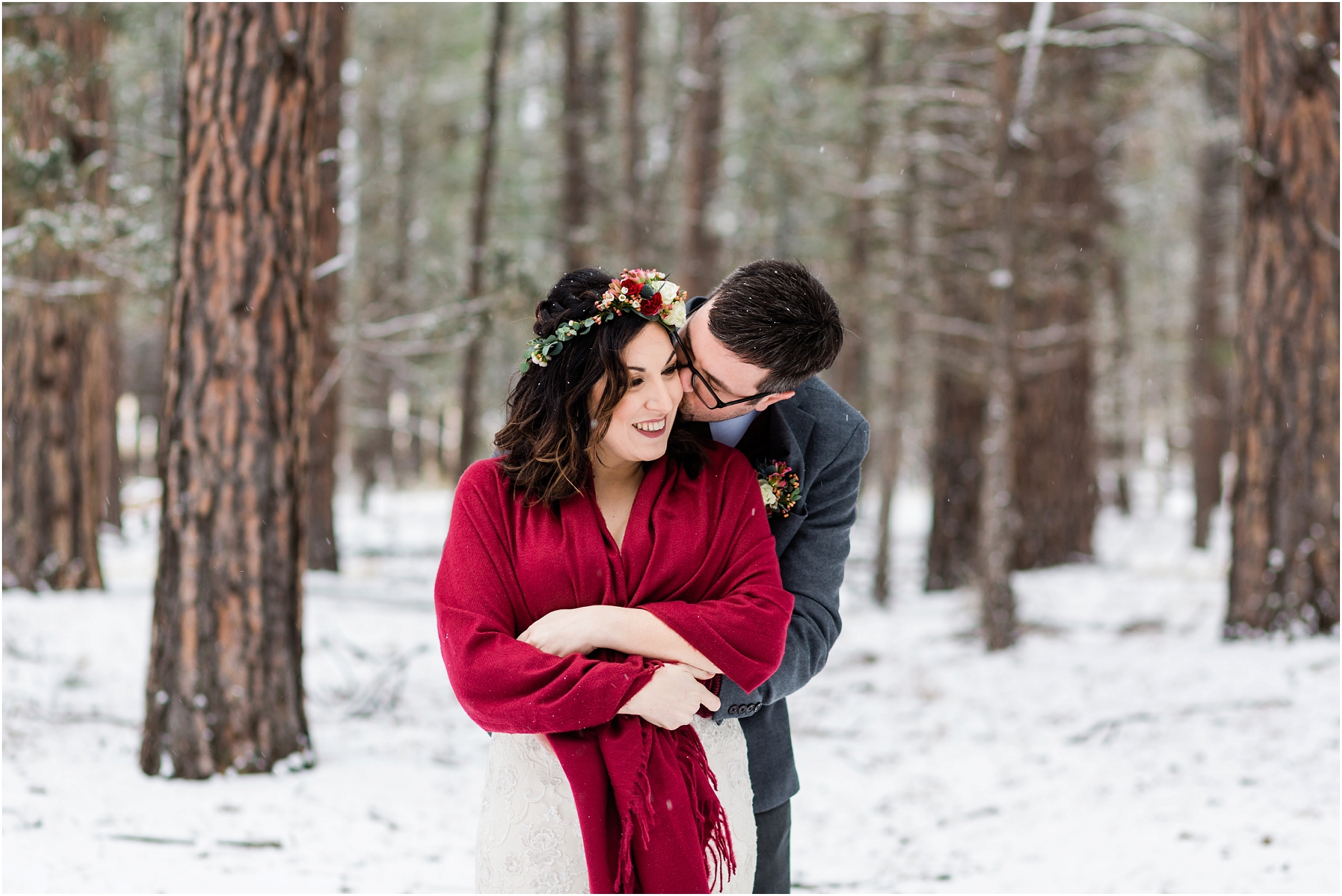 A groom snuggles up into his bride wrapped in a red shawl with snow surrounding them at their Five Pine Lodge winter elopement in Sisters, Oregon. | Erica Swantek Photography
