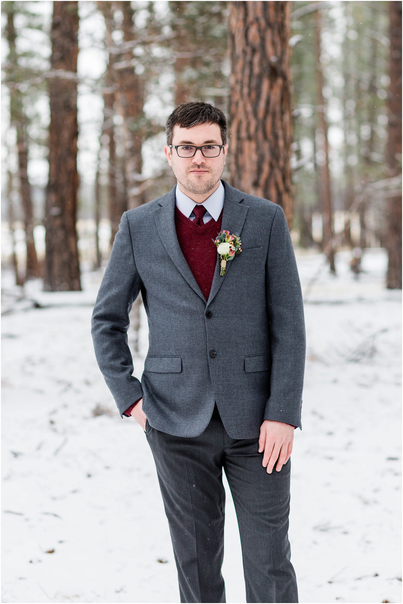 A handsome groom, wearing a gray suit with a burgundy sweater vest and tie poses in the snow covered pines at his Five Pine Lodge winter elopement in Sisters, OR. | Erica Swantek Photography