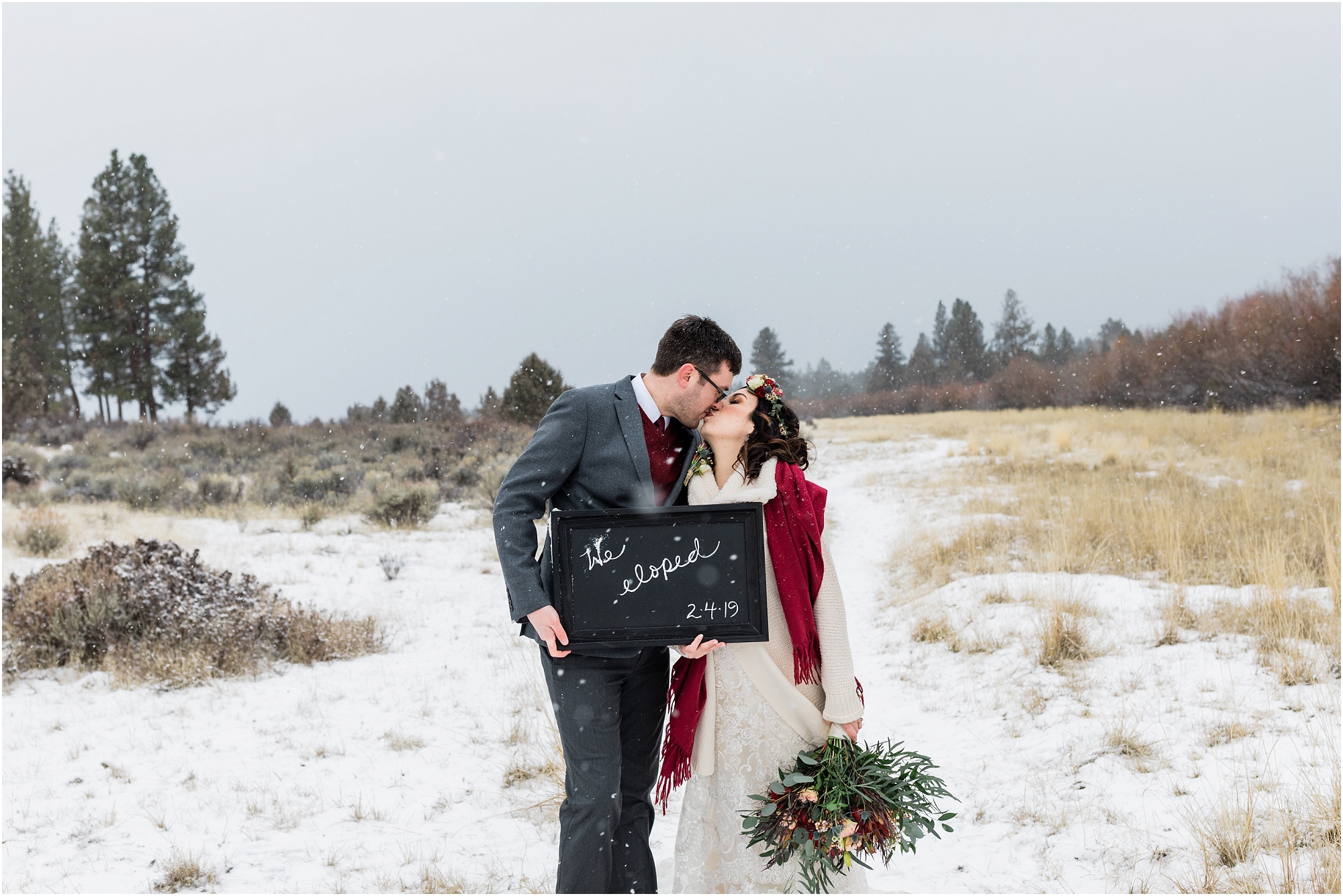 A couple poses with a chalkboard that says We Eloped as they are surrounded by a snowstorm outside of Five Pine Lodge in Sisters, Oregon. | Erica Swantek Photography