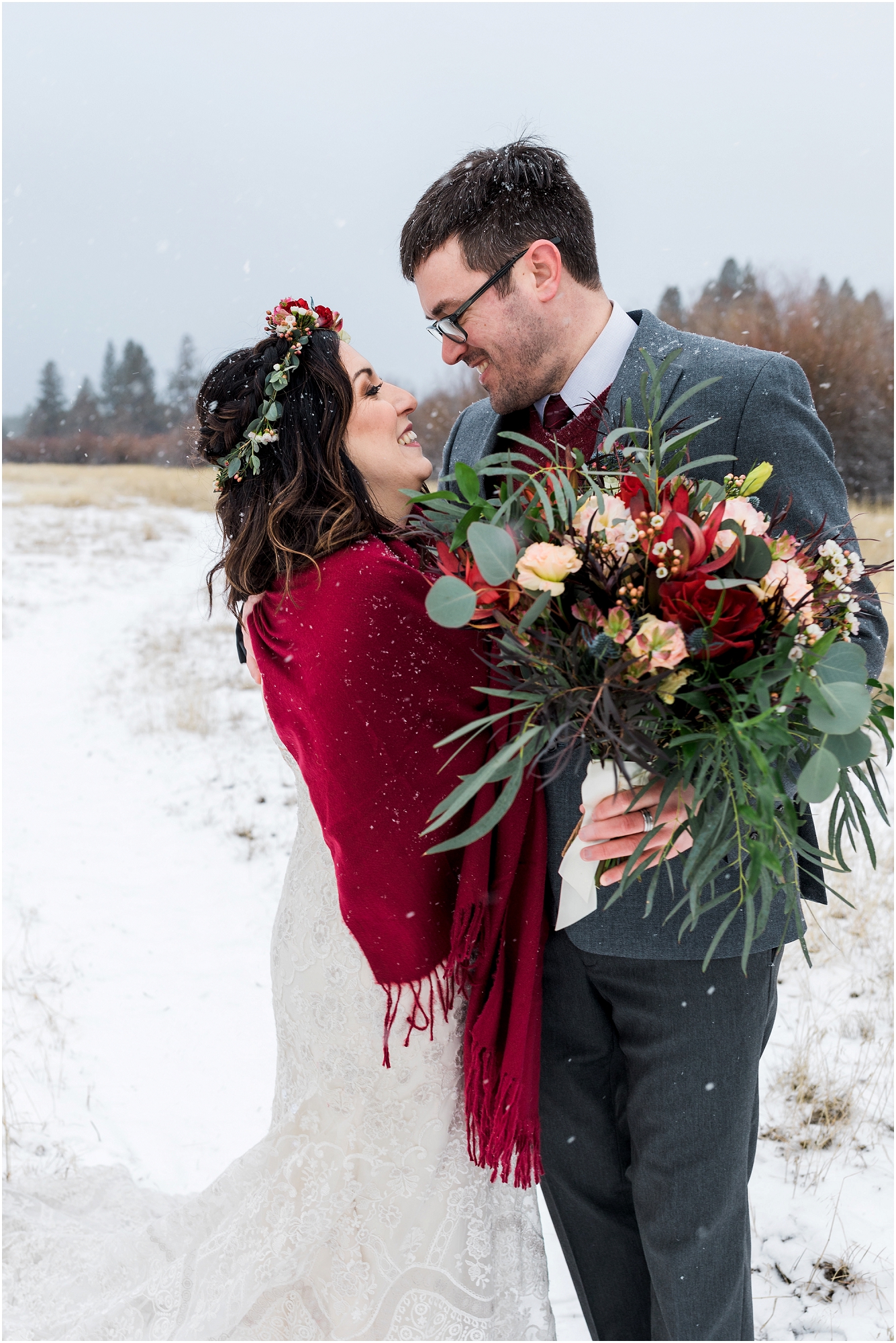 A gorgeous couple in red, burgundy and gray embrace after their outdoor Central Oregon winter elopement during a snowstorm near Five Pine Lodge in Sisters. | Erica Swantek Photography