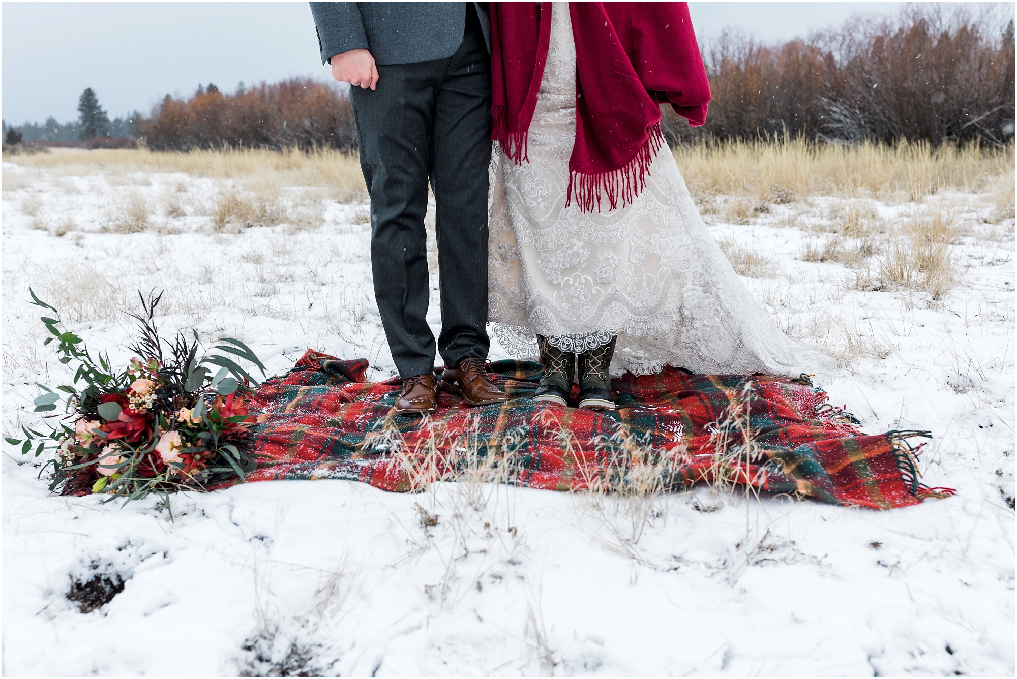 A bride, wearing gray Sorel boots and a groom in chestnut brown loafers stand on a red and green plaid blanket over the snow covered field of their Central Oregon winter elopement at Five Pine Lodge in Sisters. | Erica Swantek Photography