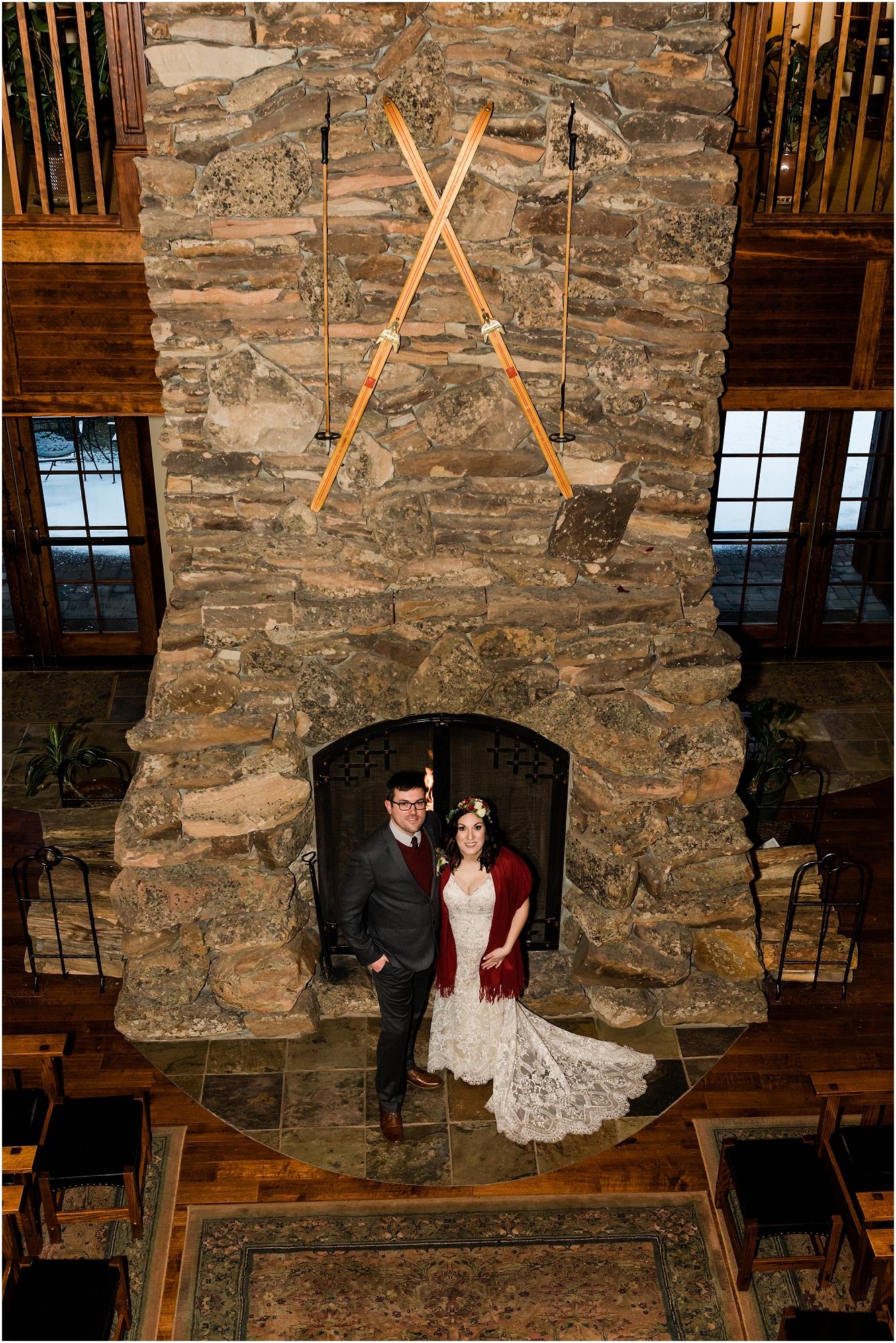 A wedding couple poses in front of the large stone fireplace decorated with wooden skis at their Central Oregon winter elopement at Five Pine Lodge in Sisters, OR. | Erica Swantek Photography