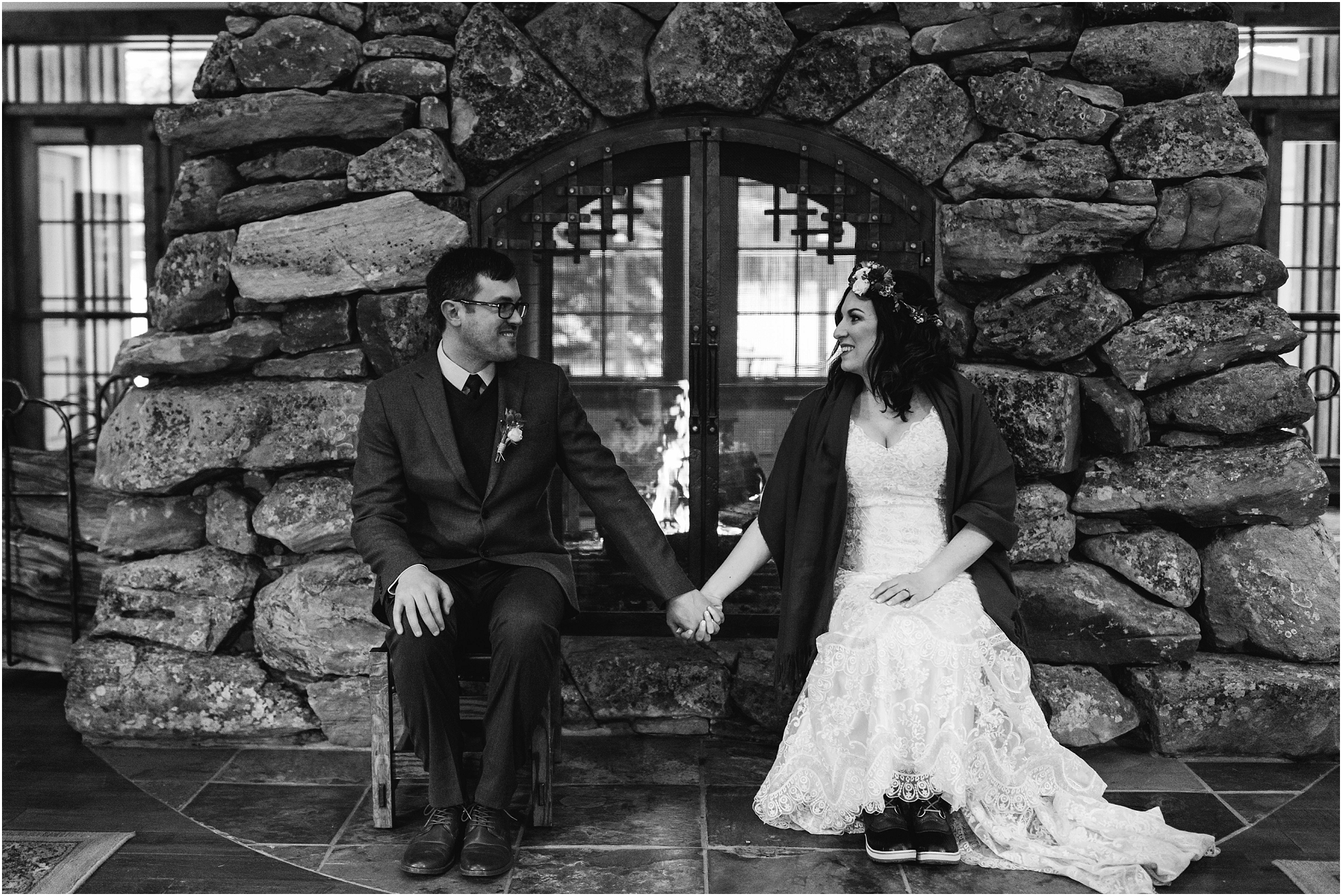 A black and white photo of a wedding couple poses in front of the large stone fireplace decorated with wooden skis at their Central Oregon winter elopement at Five Pine Lodge in Sisters, OR. | Erica Swantek Photography