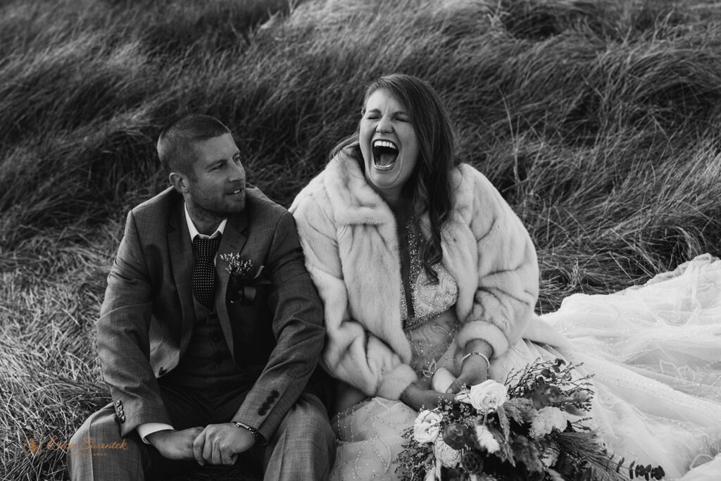 bride laughing sitting next to her new husband in a field