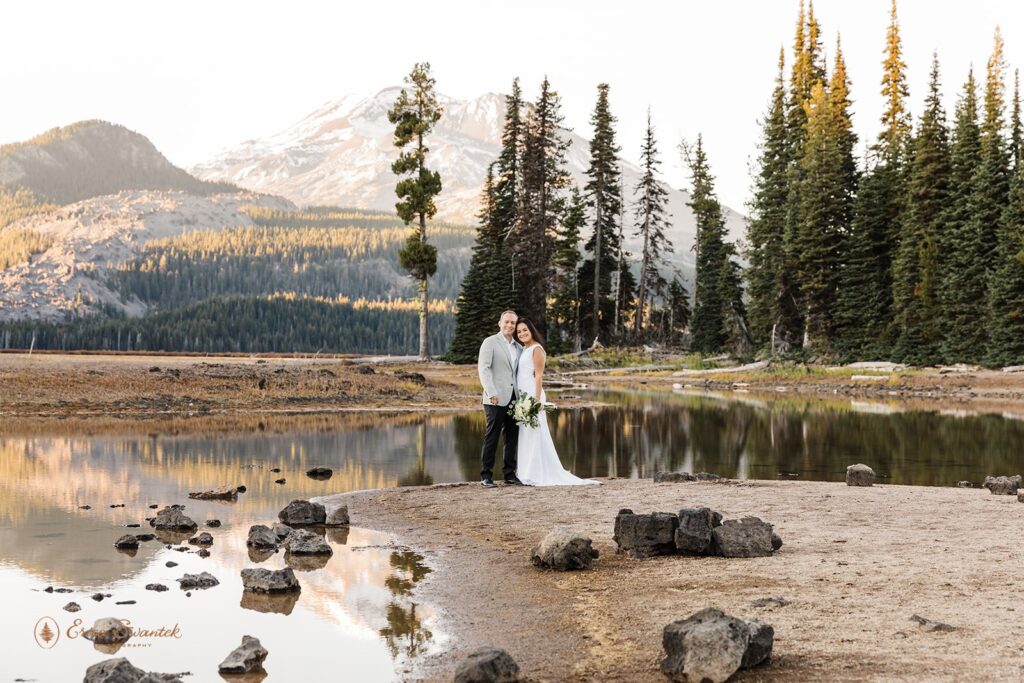 elopement couple standing by a river shore with mountain views in the background
