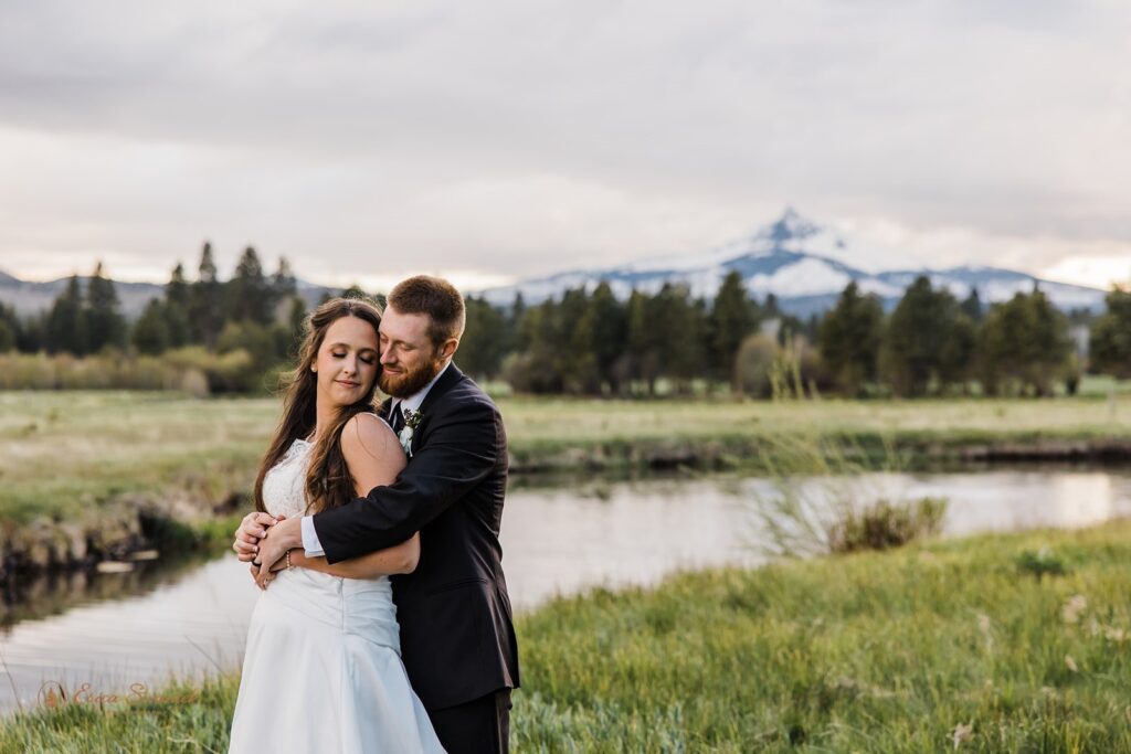 bride and groom hugging next to a large lake with mountain views at the black butte ranch
