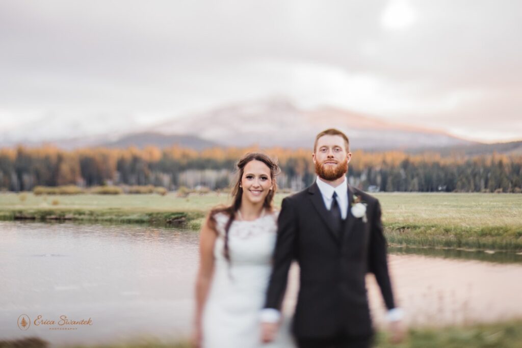bride and groom holding hands next to a large lake with mountain views at the black butte ranch