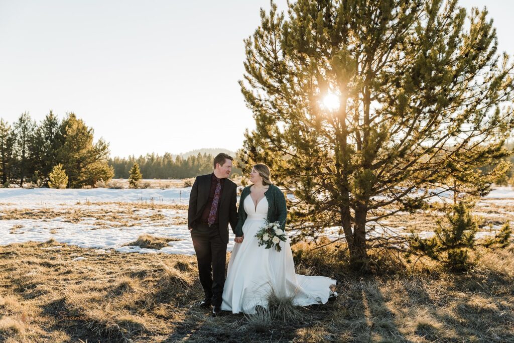 bride and groom walking hand in hand through the snow during their elopement in sunriver, oregon