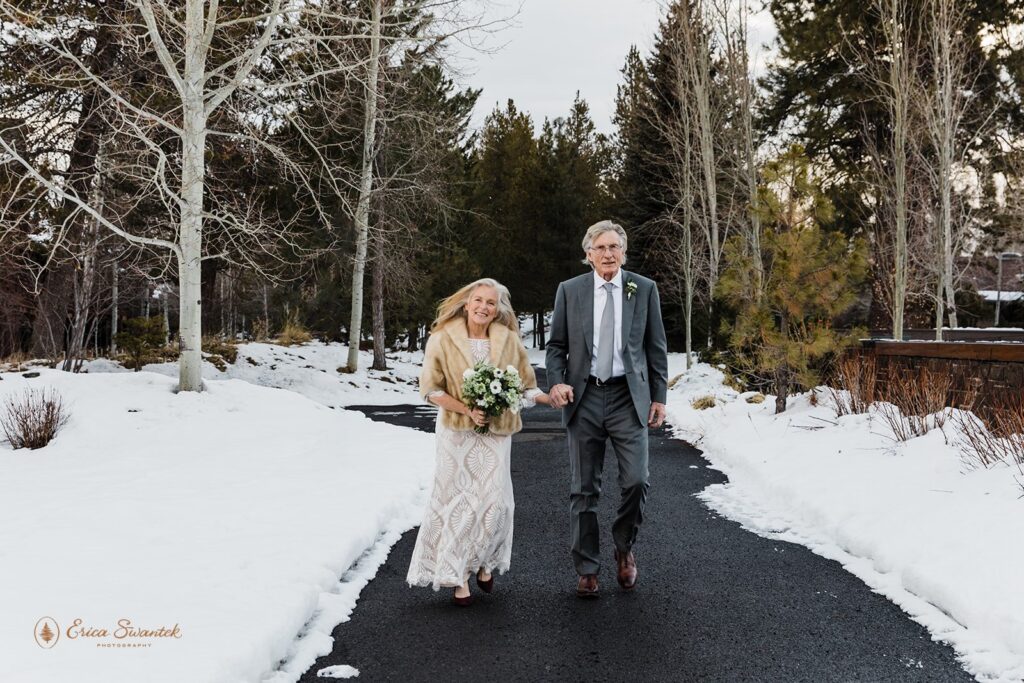 older elopement couple walking hand in hand on a road lined with snowy piles