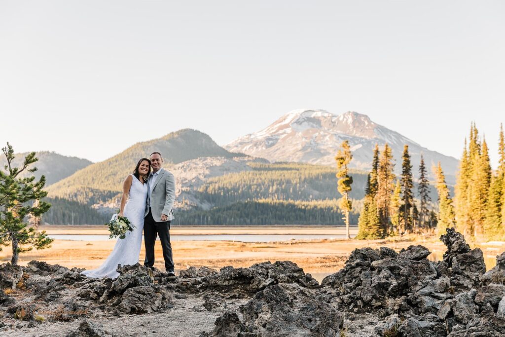 smiling elopement couple standing on a rocky terrain with mountain views in the backdrop 
