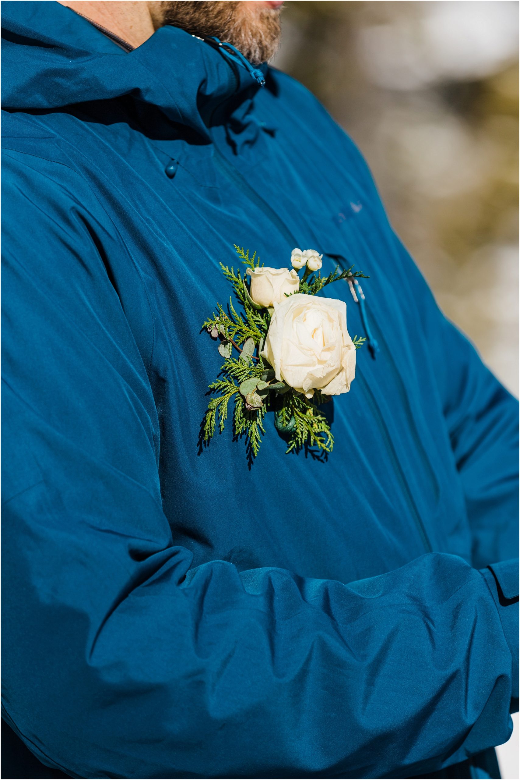 A groom wearing a cobalt blue ski jacket has a white rose and green pine bough boutonniere during his Mt Bachelor adventure elopement ceremony in Oregon. | Erica Swantek Photography