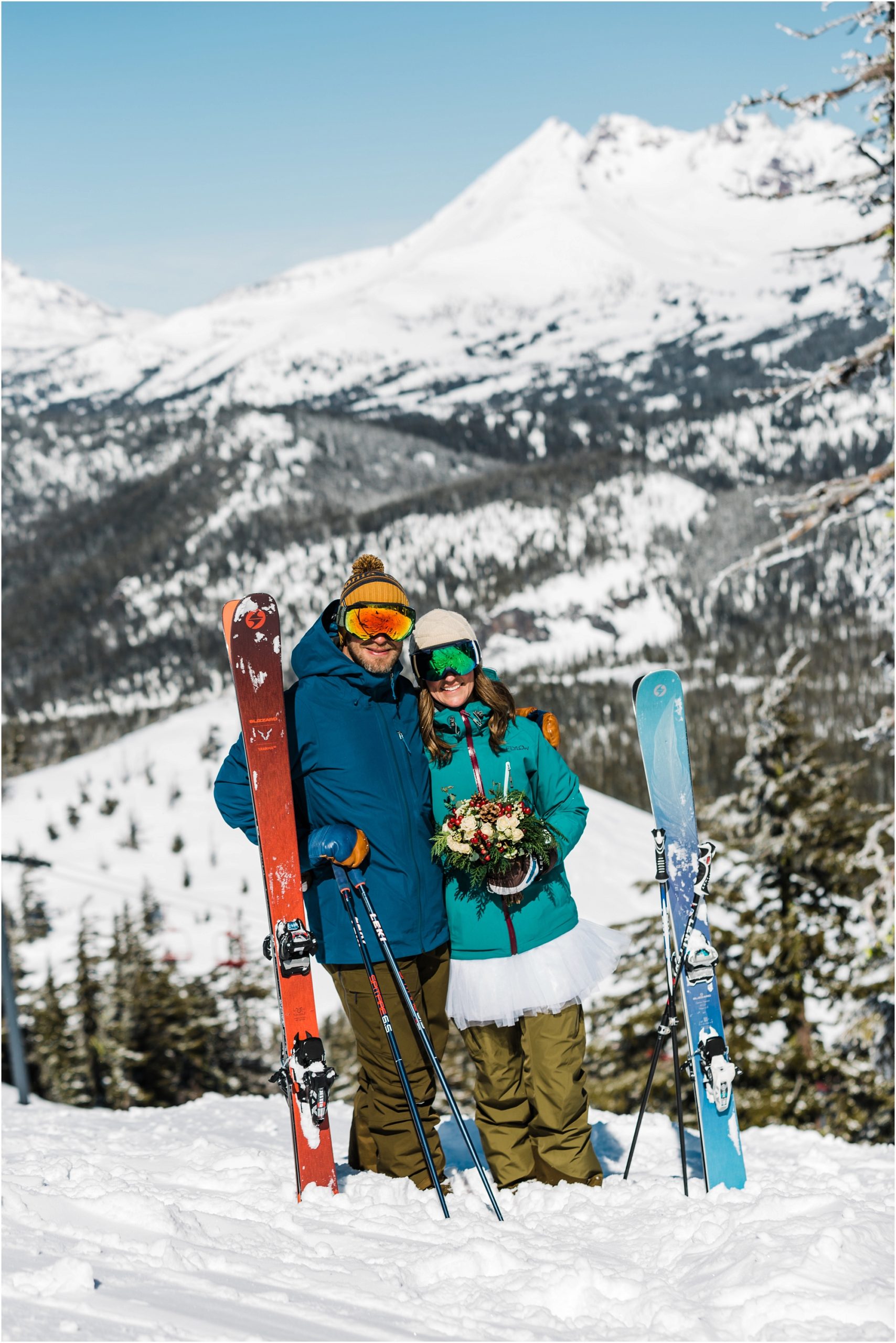 A couple poses with their skis in front of the mountains at their Mt Bachelor ski resort wedding in Bend, Oregon. | Erica Swantek Photography