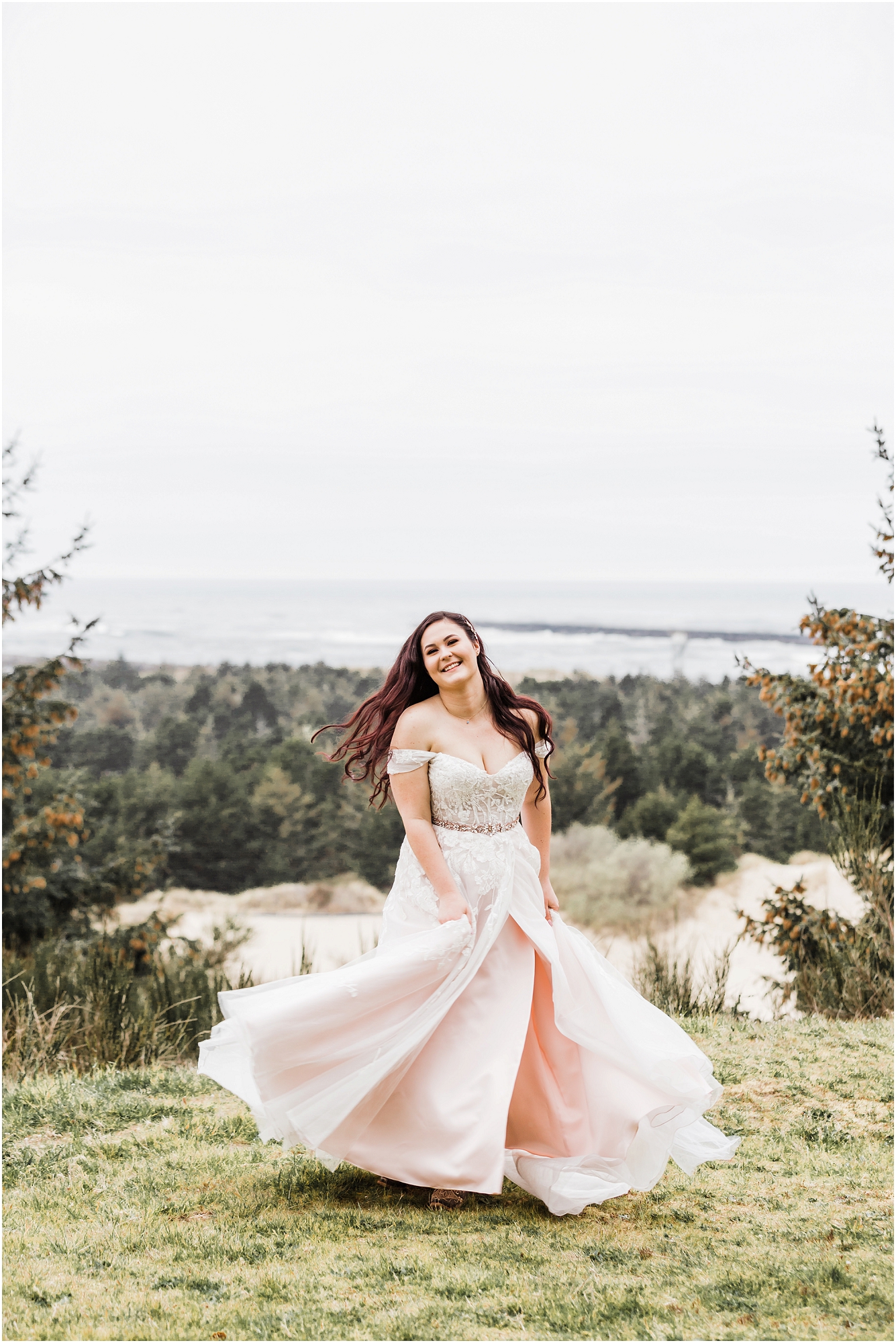 A gorgeous bride, wearing a blush pink gown spins in the grass above the ocean at her Oregon Coast Guard Elopement near Winchester Bay, Oregon. | Erica Swantek Photography