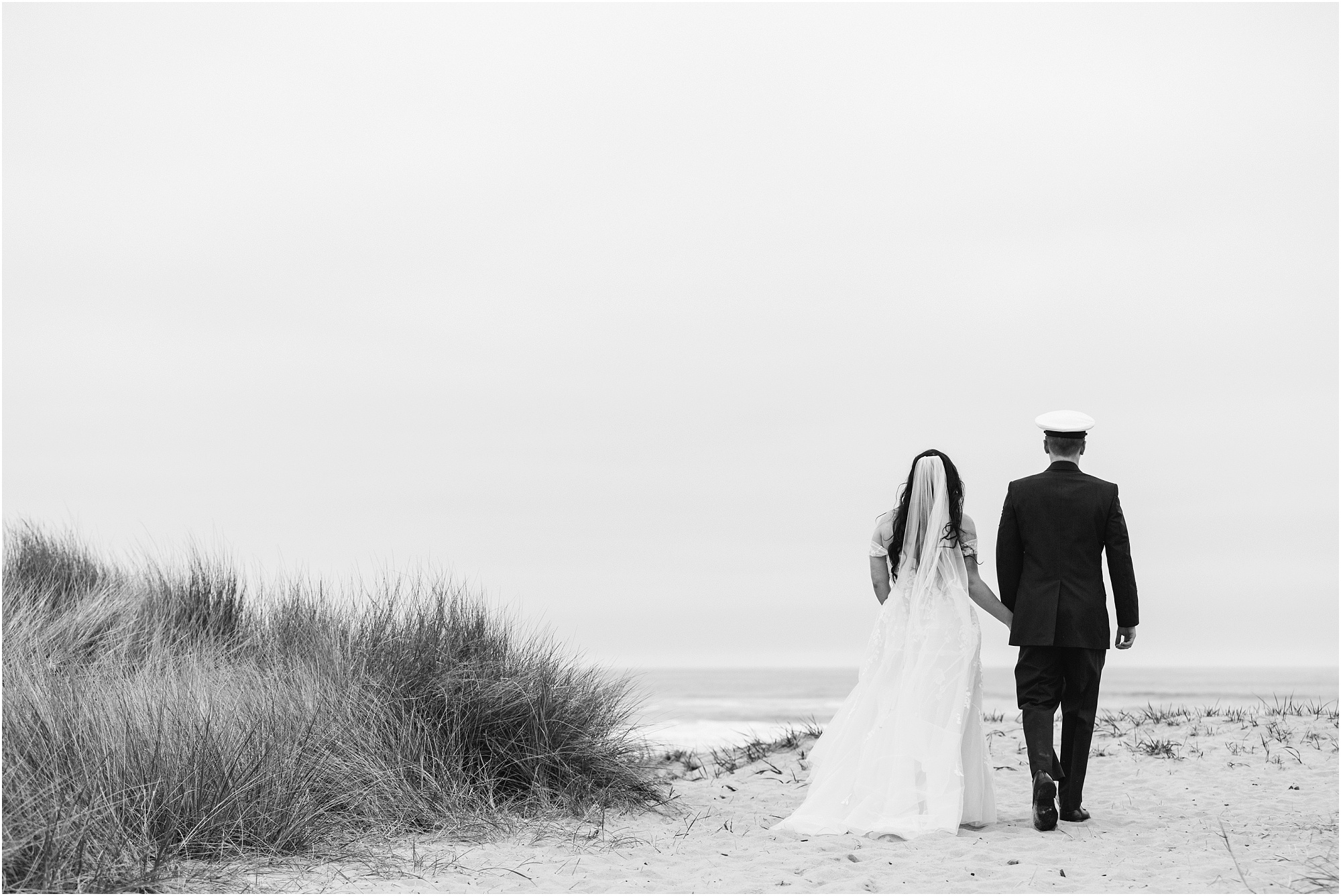 A black and white image of a bride and groom walking away from the camera towards the ocean for their adventure elopement along the Oregon Coast. | Erica Swantek Photography