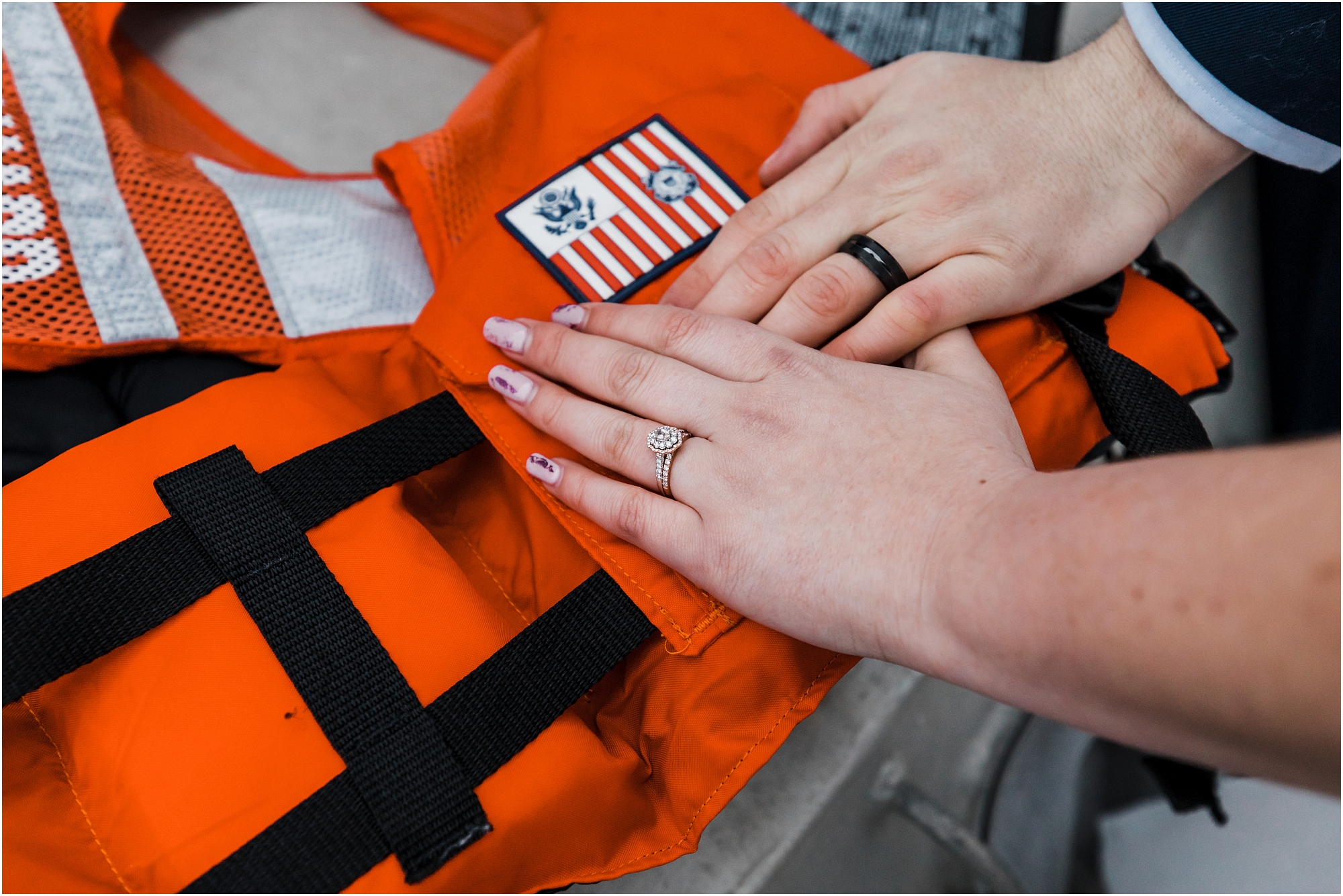Wedding bands on the hands of the bride and groom, resting on a orange life jacket, which was used for their Oregon Coast Guard elopement. | Erica Swantek Photography