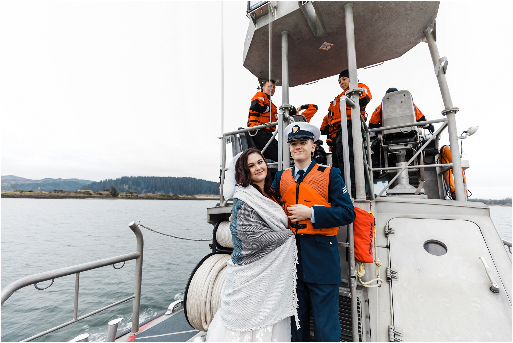 A bride and groom, both wearing bright orange life jackets, ride on the deck of a US Coast Guard ship as we portage out to sea for their adventure elopement in Oregon. | Erica Swantek Photography