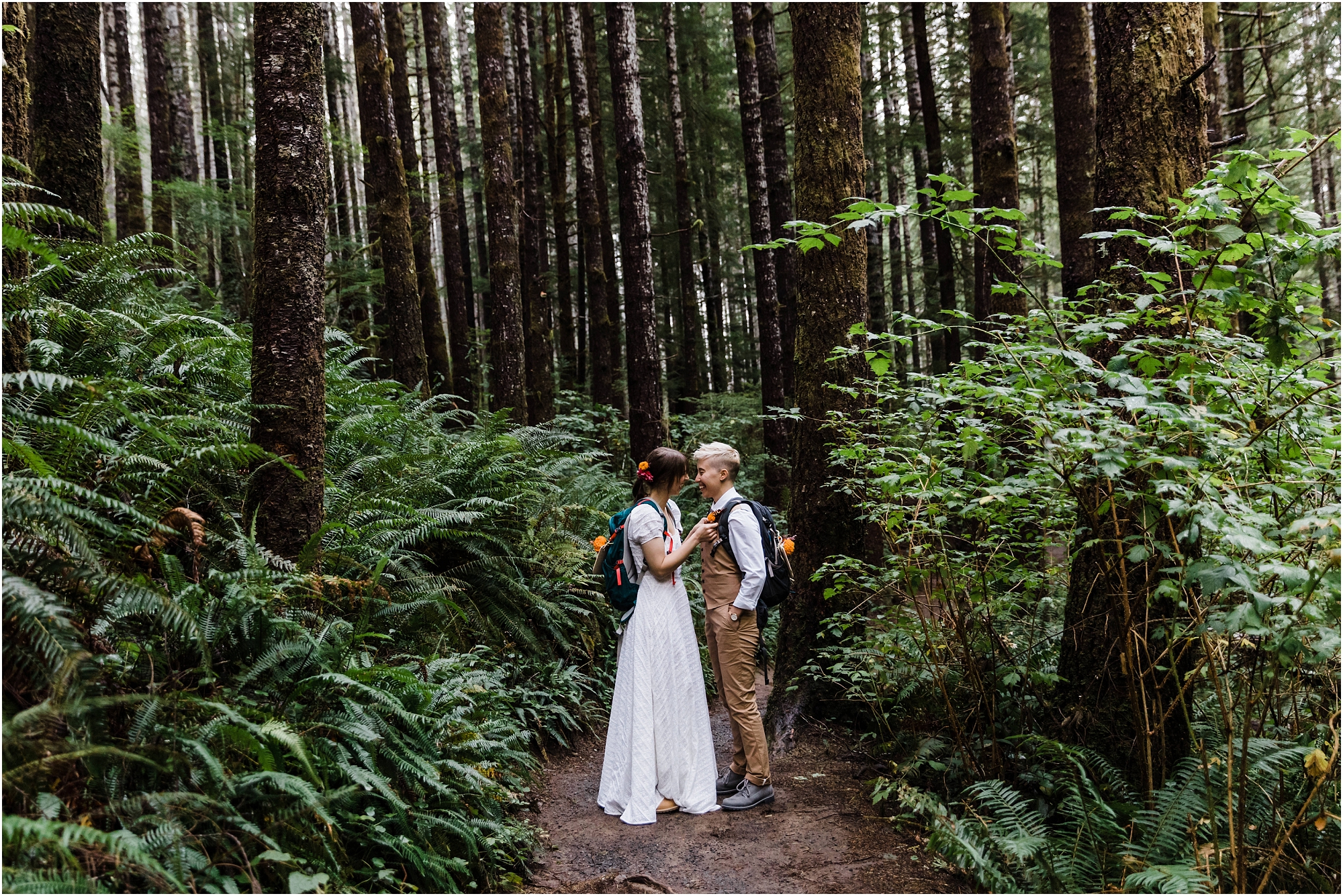 A wedding couple, stands among the tall spruce trees and lush ferns on the trail to their waterfall elopement near the Oregon Coast. | Erica Swantek Photography