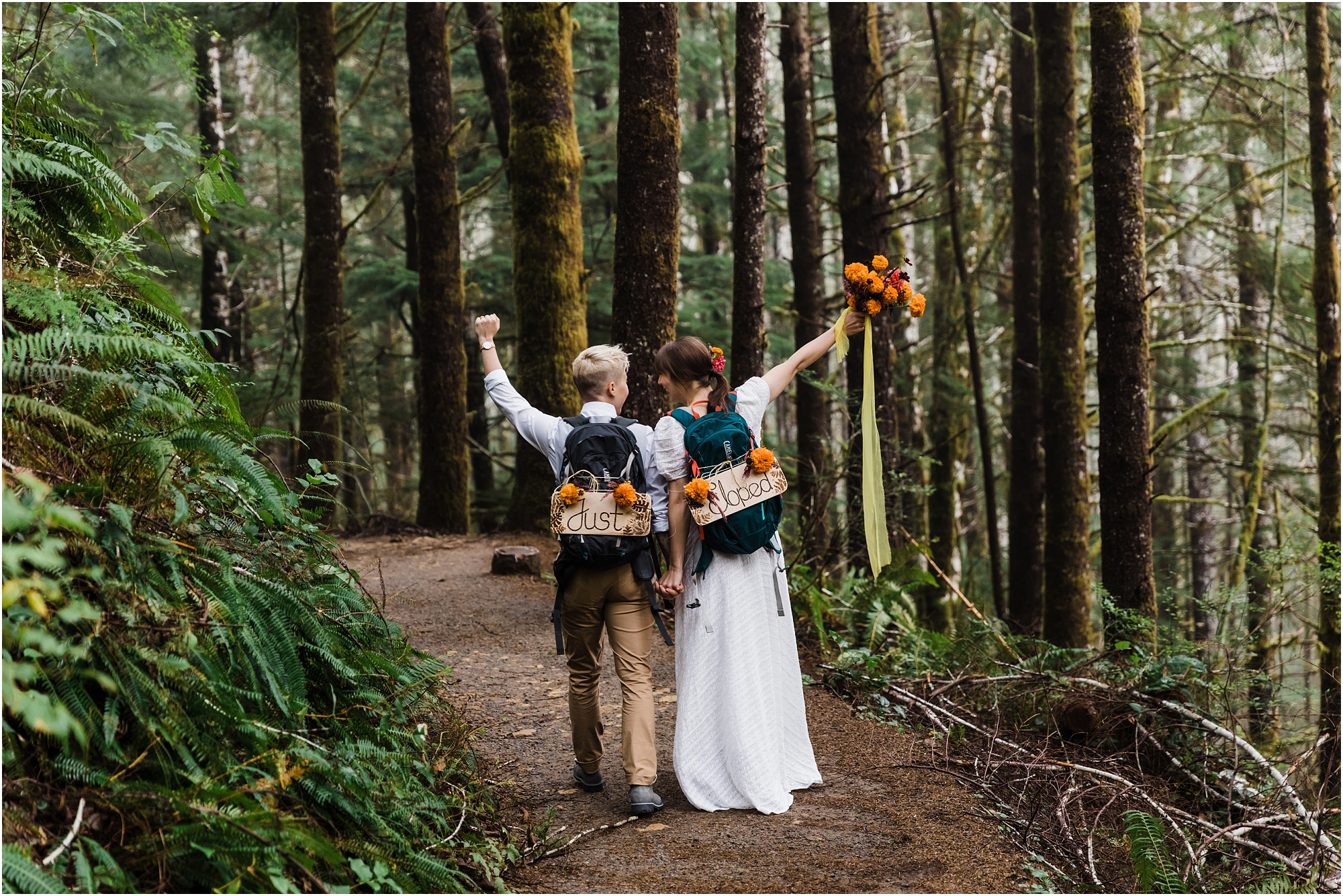 A couple does a celebratory fist pump while wearing their Just Eloped backpacks for their Oregon adventure elopement day. | Erica Swantek Photography