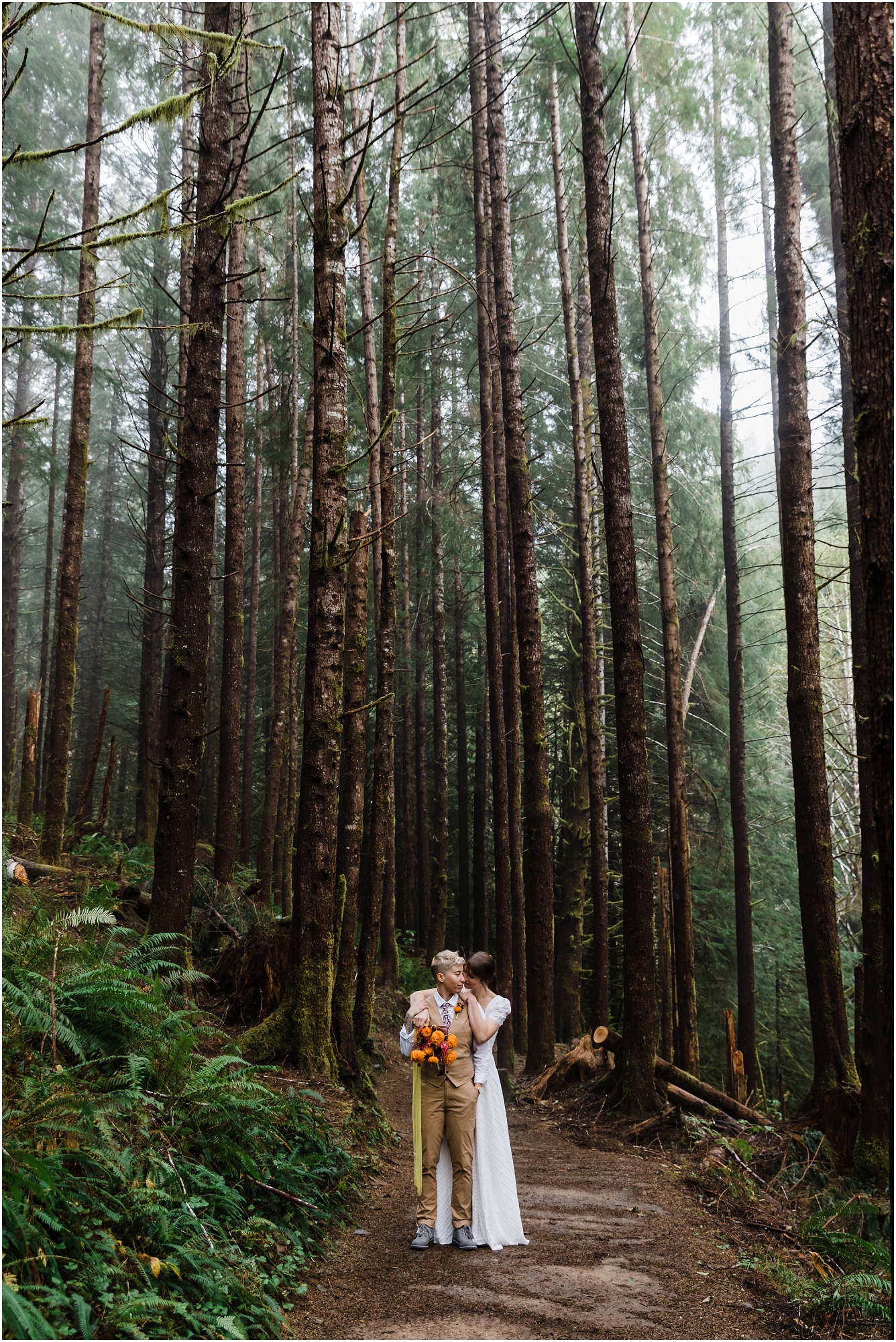 A gorgeous couple stands in the dense, dark forest covered in green ferns wearing their wedding attire for their PNW hiking elopement. | Erica Swantek Photography