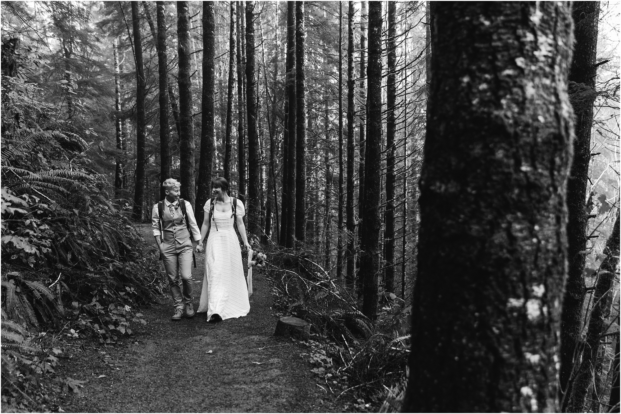 A beautiful black and white image of a couple hiking in their wedding clothes on the way to their ceremony location for their PNW waterfall elopement. | Erica Swantek Photography