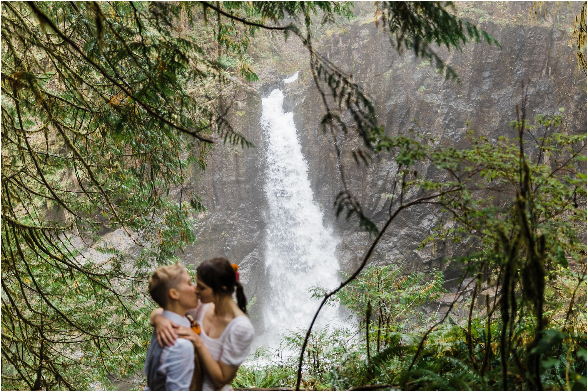 A LGBTQ+ couple kisses in front of Drift Creek falls in Oregon during their PNW hiking adventure elopement. | Erica Swantek Photography