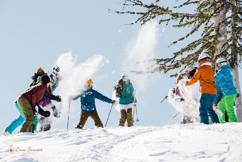 bride and groom skiing down the mountain at mt bachelor with friends throwing snow at them